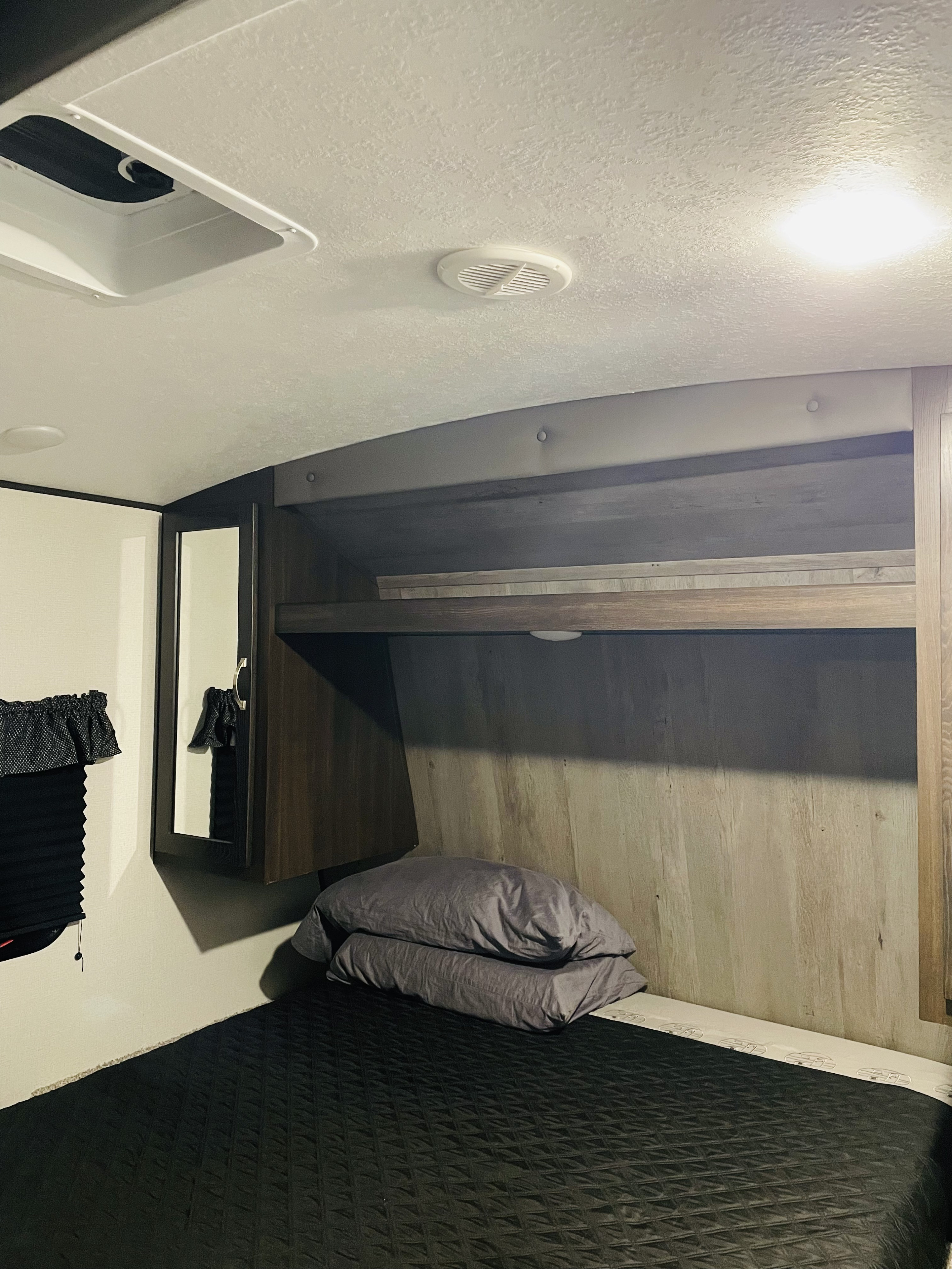 Cozy RV rental bedroom featuring dark bedding, overhead storage, mirror, and air vent, ready for comfortable travel.. Keystone Springdale 2021