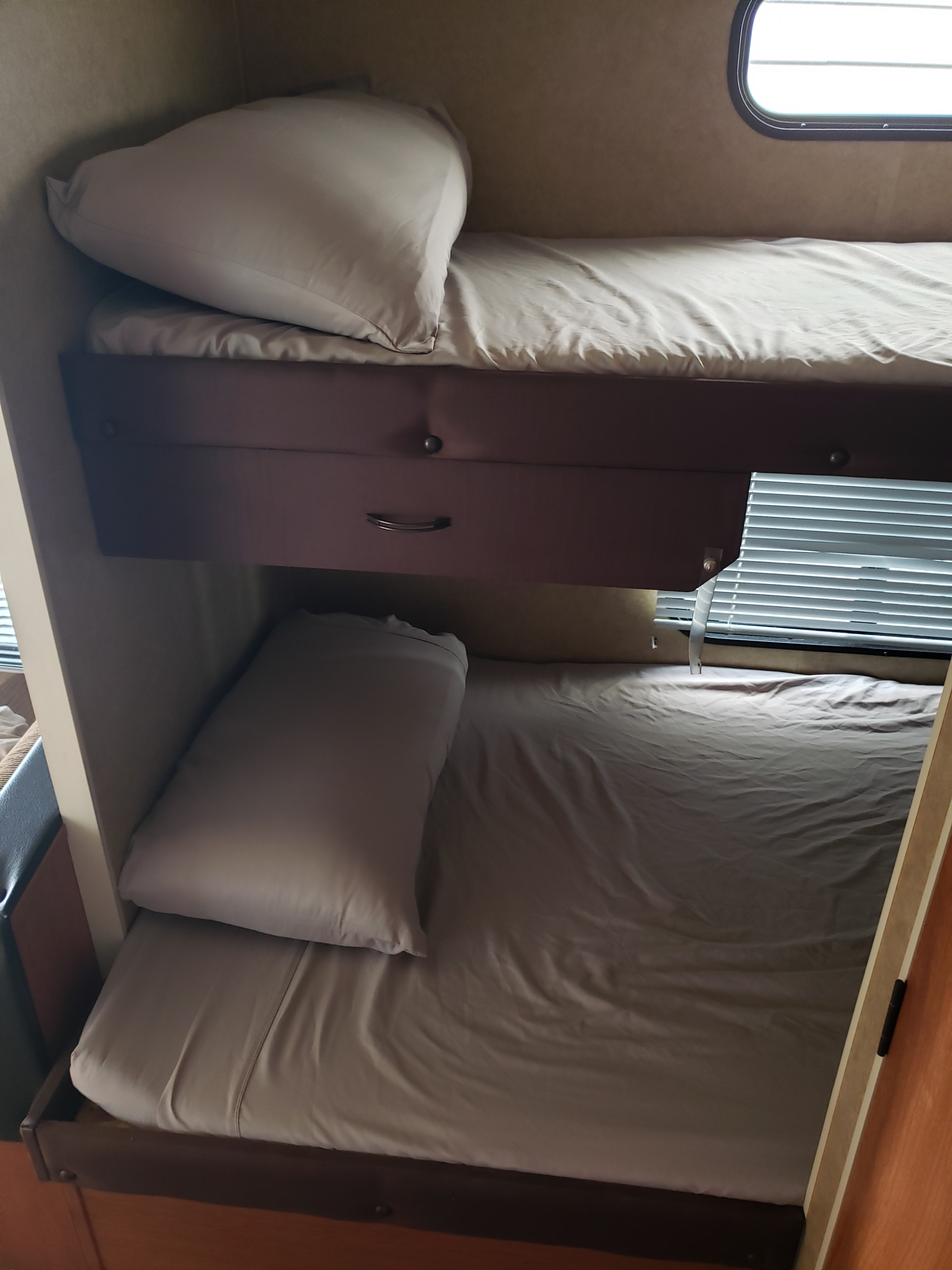 Cozy bunk beds with neutral bedding and pillows inside an RV rental, featuring a small storage drawer and window blinds.. Forest River Cherokee Grey Wolf 2013