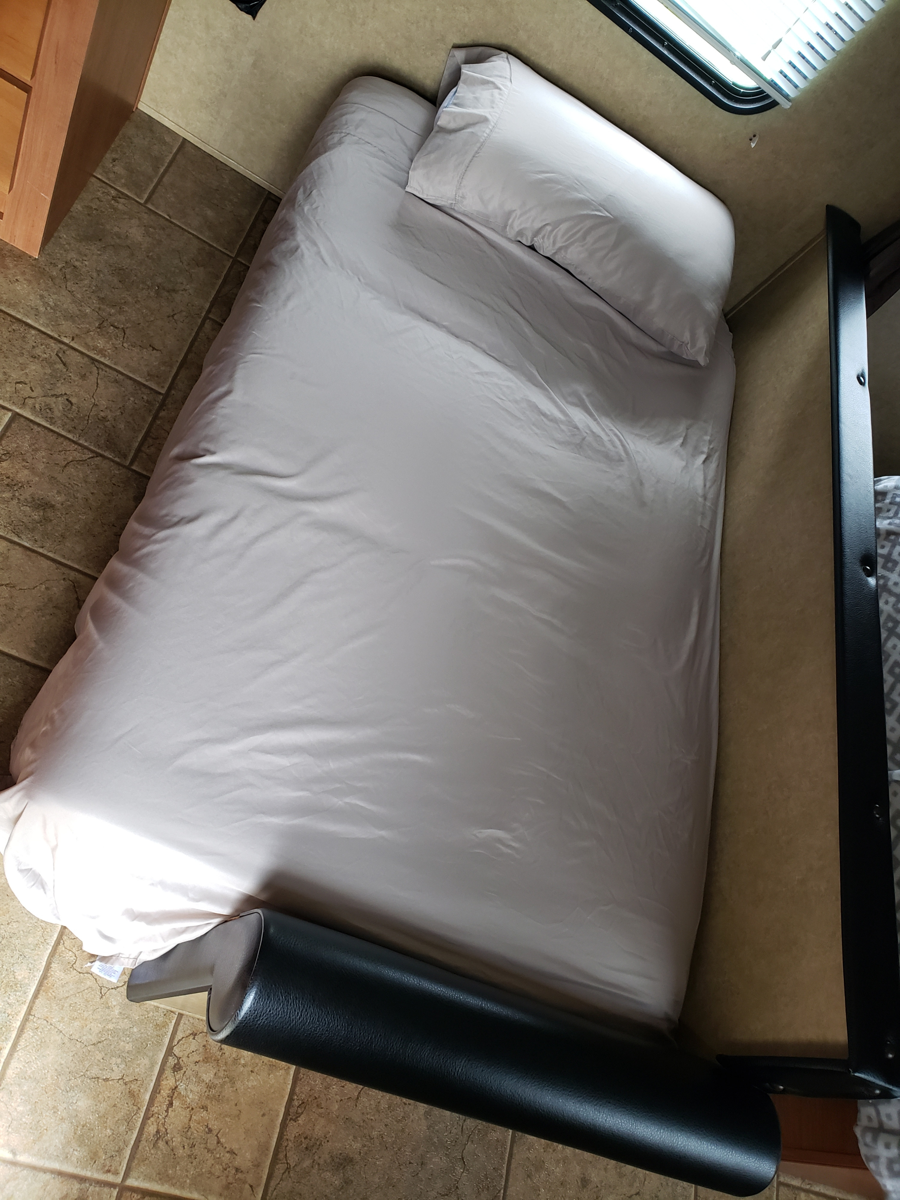 An RV rental's bedroom area, featuring a light-sheeted bed with a pillow, wooden cabinet, tiled floor, and a black bolster at the foot.. Forest River Cherokee Grey Wolf 2013