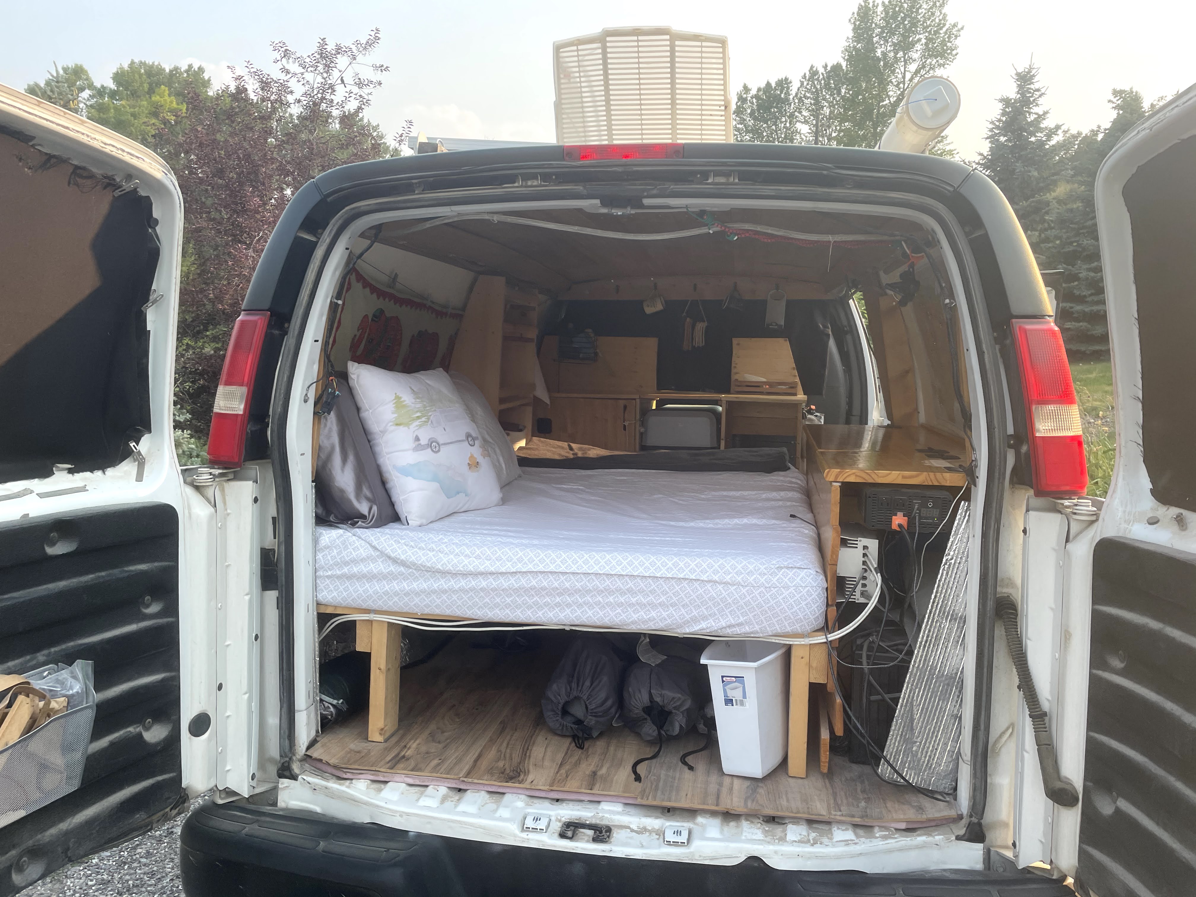 Explore this custom rv rental van with its bed, built-in storage, and off-grid power setup, seen from the open rear doors.. Chevrolet Other 2013