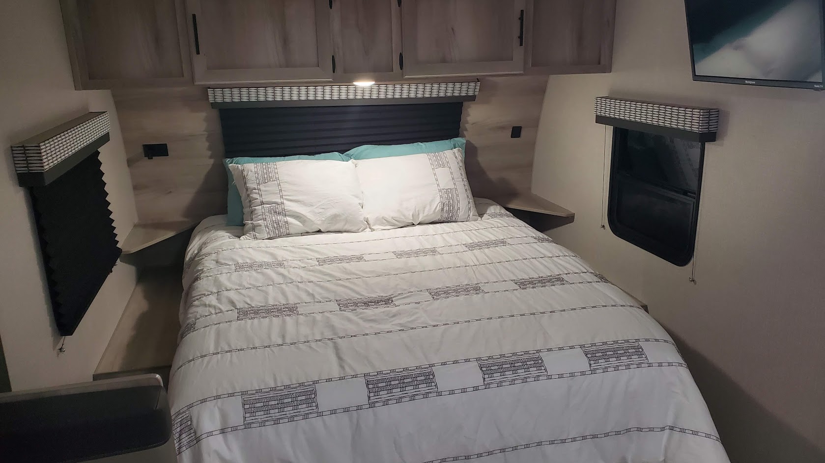 Cozy RV rental bedroom featuring a comfortable bed with white bedding, built-in overhead cabinets, and window blinds.. Other Other 2021