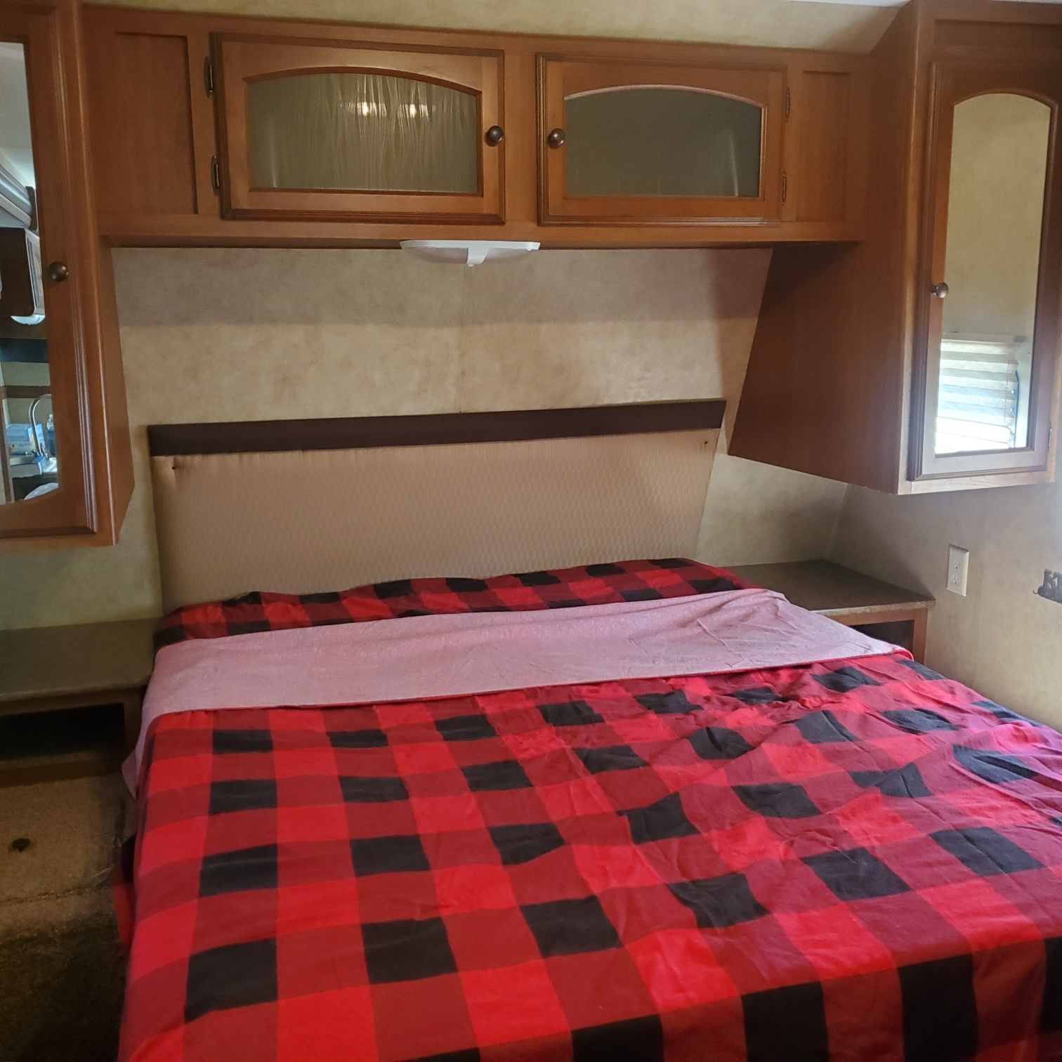 RV rental bedroom featuring a cozy red & black plaid bed, padded headboard, & ample wooden cabinets.. Dutchmen Dutchmen 2012