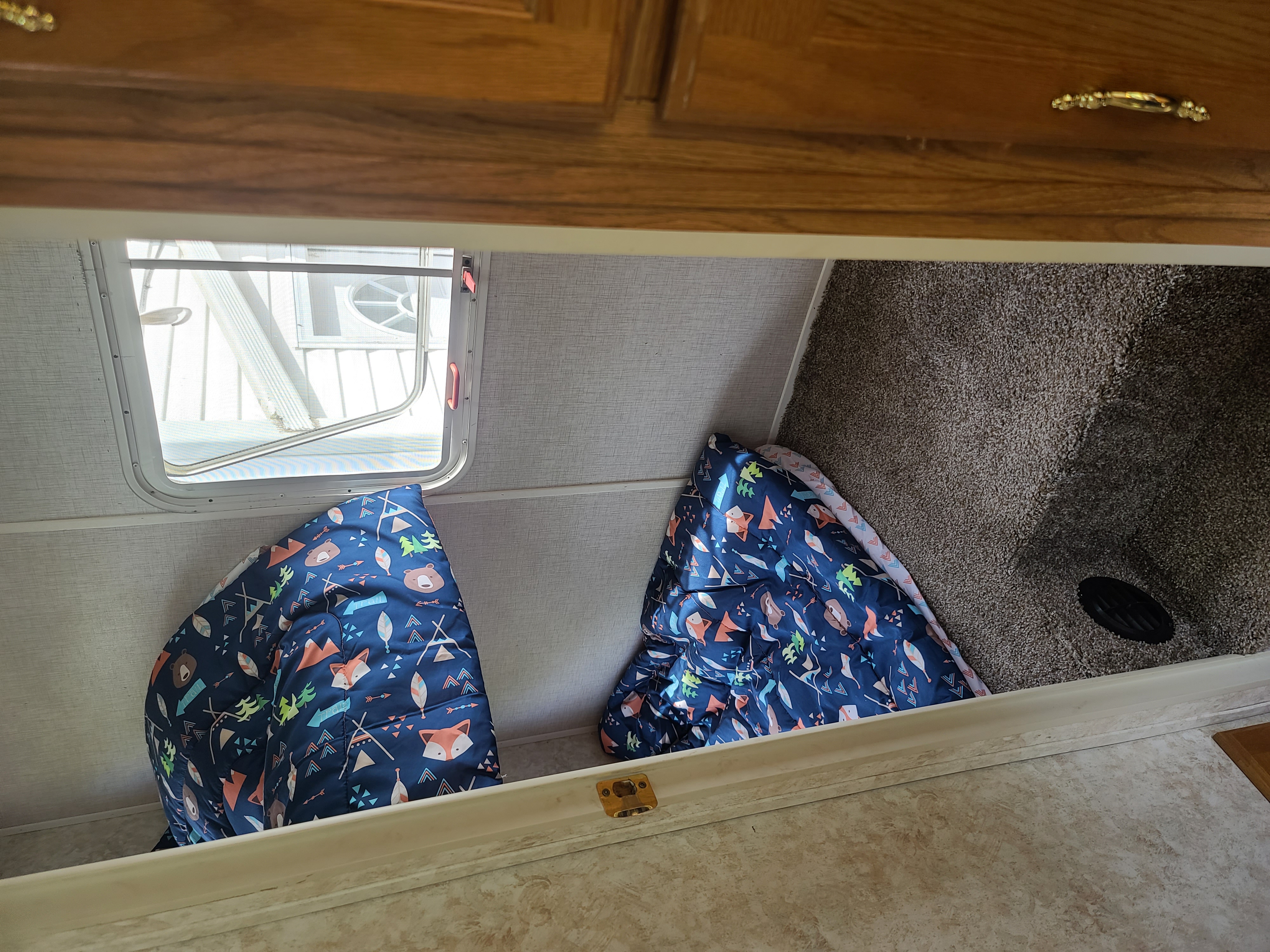 View into an RV rental sleeping area featuring two patterned sleeping bags, a window, and soft carpet.. Wildwood Wildwood LE 2006