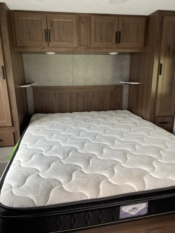 Clean RV rental bedroom with a comfy mattress, wooden headboard, and overhead/side storage for travel.. Forest River Sunseeker 2020
