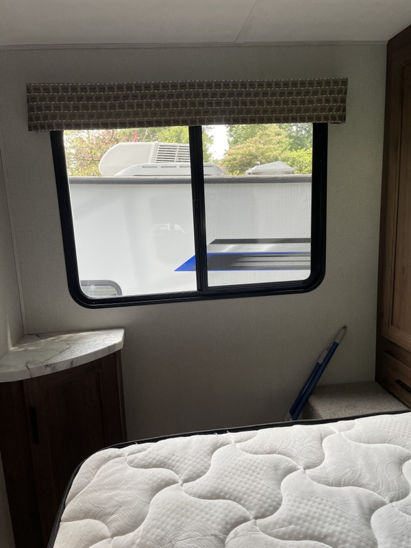Bedroom in an RV rental with a quilted mattress, a window revealing another RV outside, and a built-in corner cabinet.. Forest River Sunseeker 2020