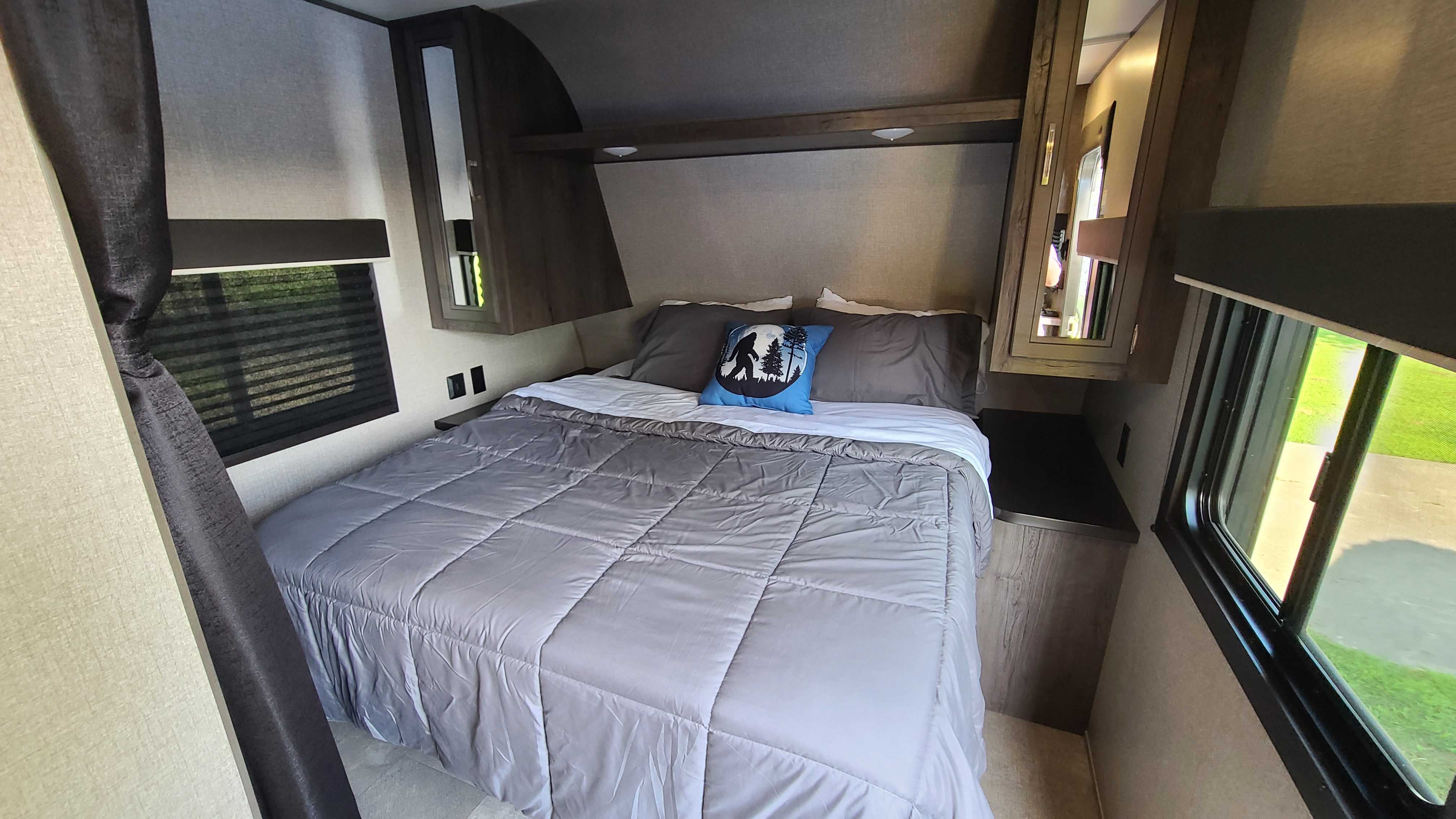 Inside a comfortable RV rental bedroom, featuring a large bed, overhead cabinets, and side windows with blinds.. Jayco Jay Flight 2021