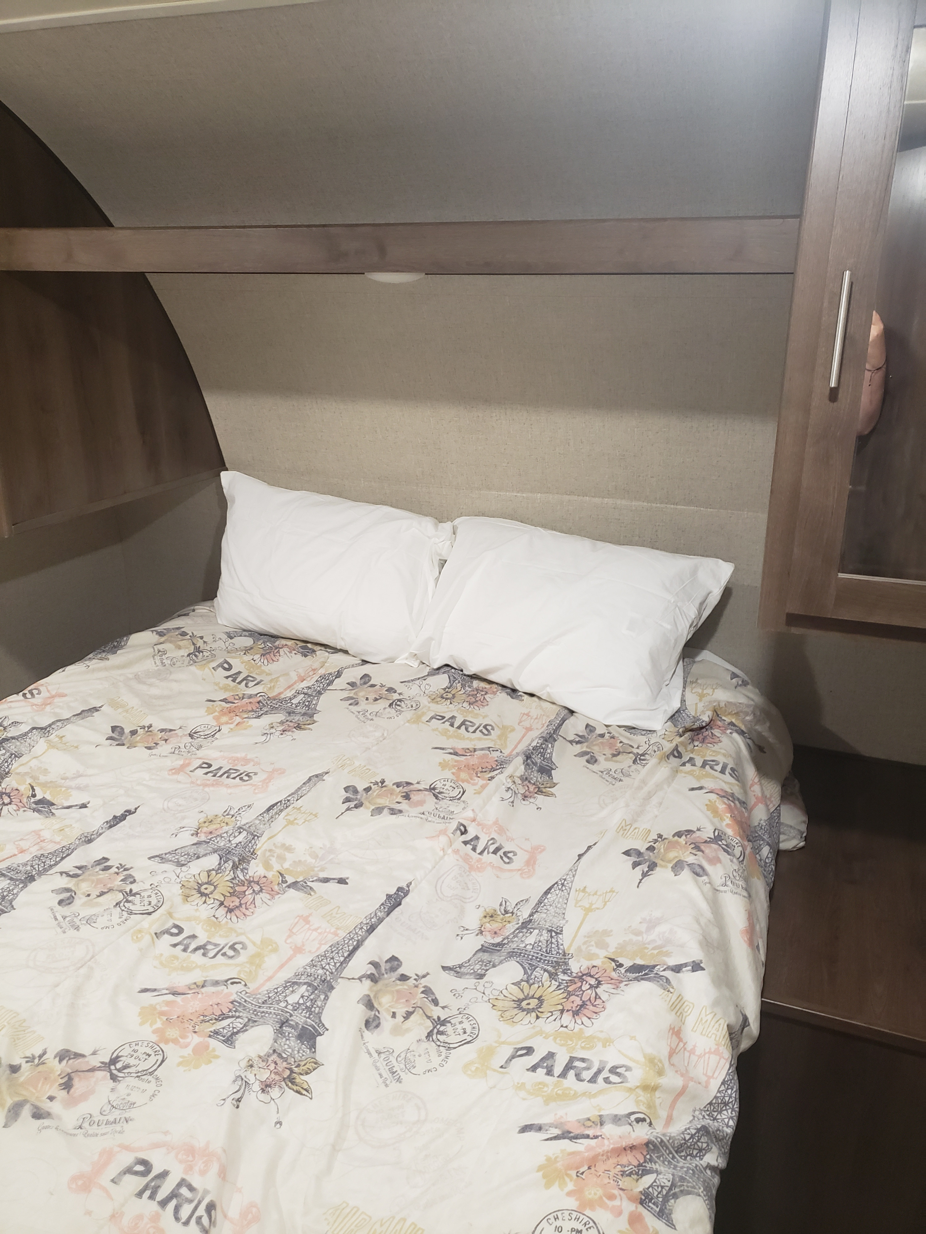 Inside an RV rental: a cozy bedroom featuring a bed with white pillows and a Paris-themed comforter with Eiffel Tower designs.. Shasta Oasis 2019