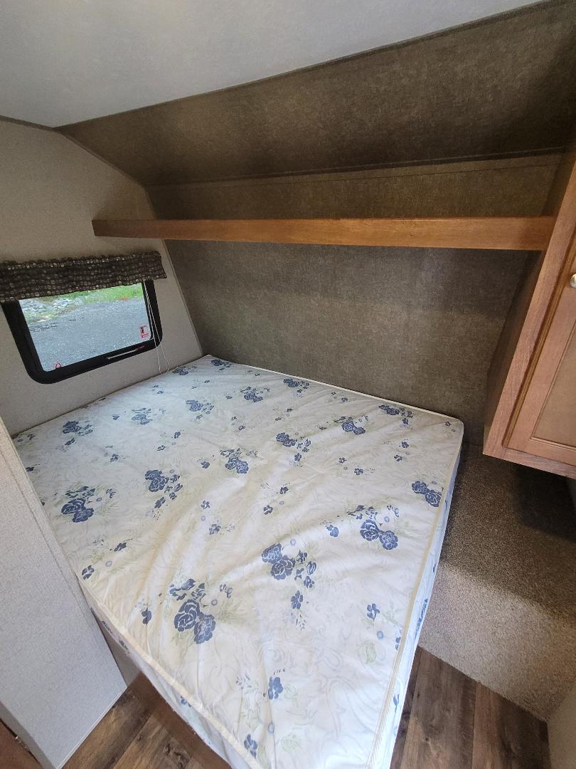 RV rental bedroom: Cozy interior featuring a bed with floral mattress, window, overhead shelf, and cabinet.. Keystone Summerland 2017