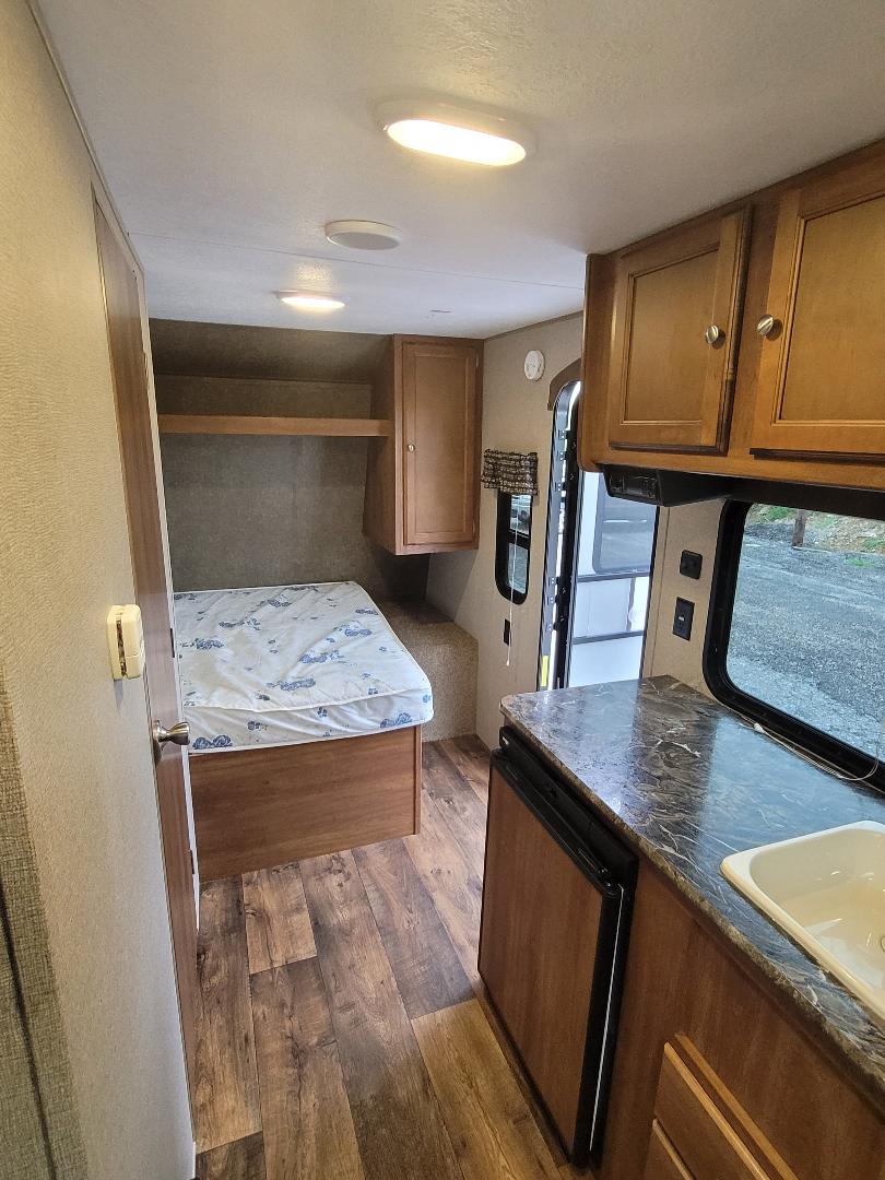 Inside this RV rental: a bright interior with a comfortable bed, wood flooring, and a compact kitchen counter with sink and fridge.. Keystone Summerland 2017