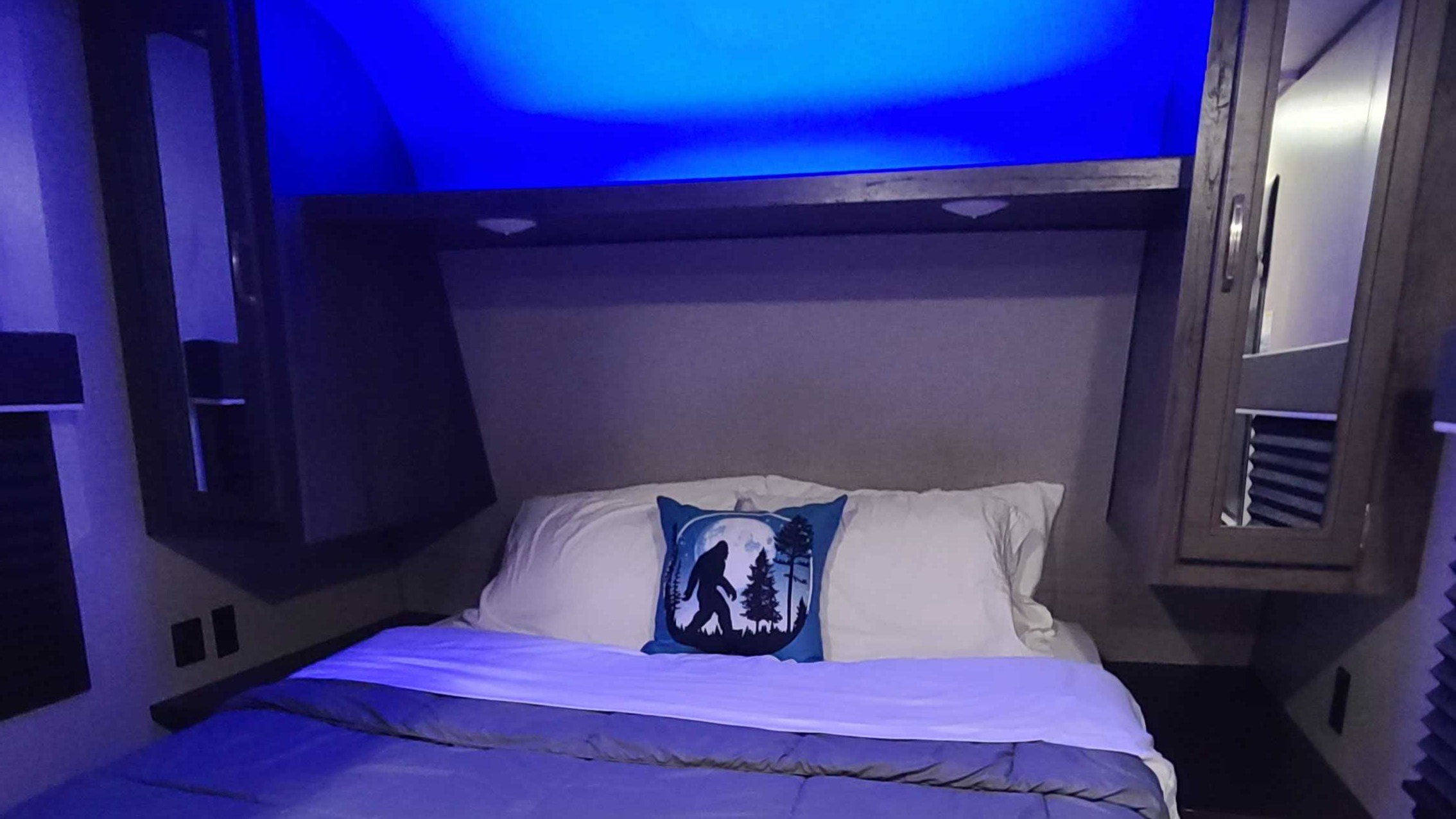 Cozy RV rental bedroom with blue LED lighting, a comfortable bed, and a fun Bigfoot pillow for your travels.. Jayco Jay Flight 2021