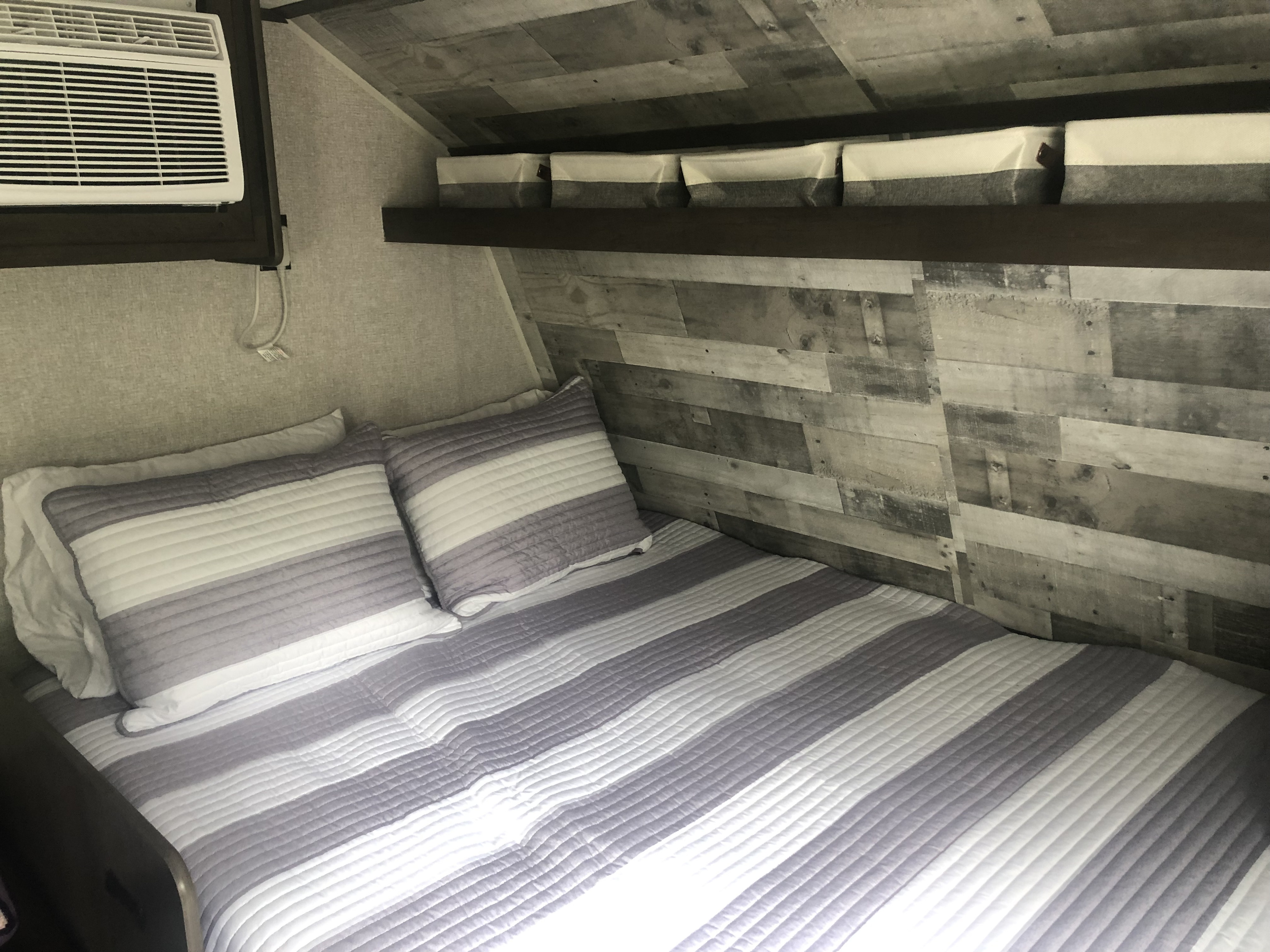 Cozy RV rental bedroom with striped bedding, AC, and storage bins above the bed.. Dutchmen Coleman 2021