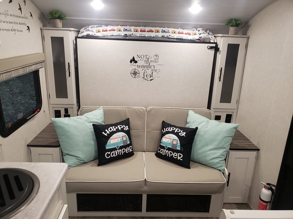 Discover a cozy RV rental interior: sofa with "Happy Camper" pillows, light blue cushions, and a clever fold-up bed system.. Forest River R-Pod 2022