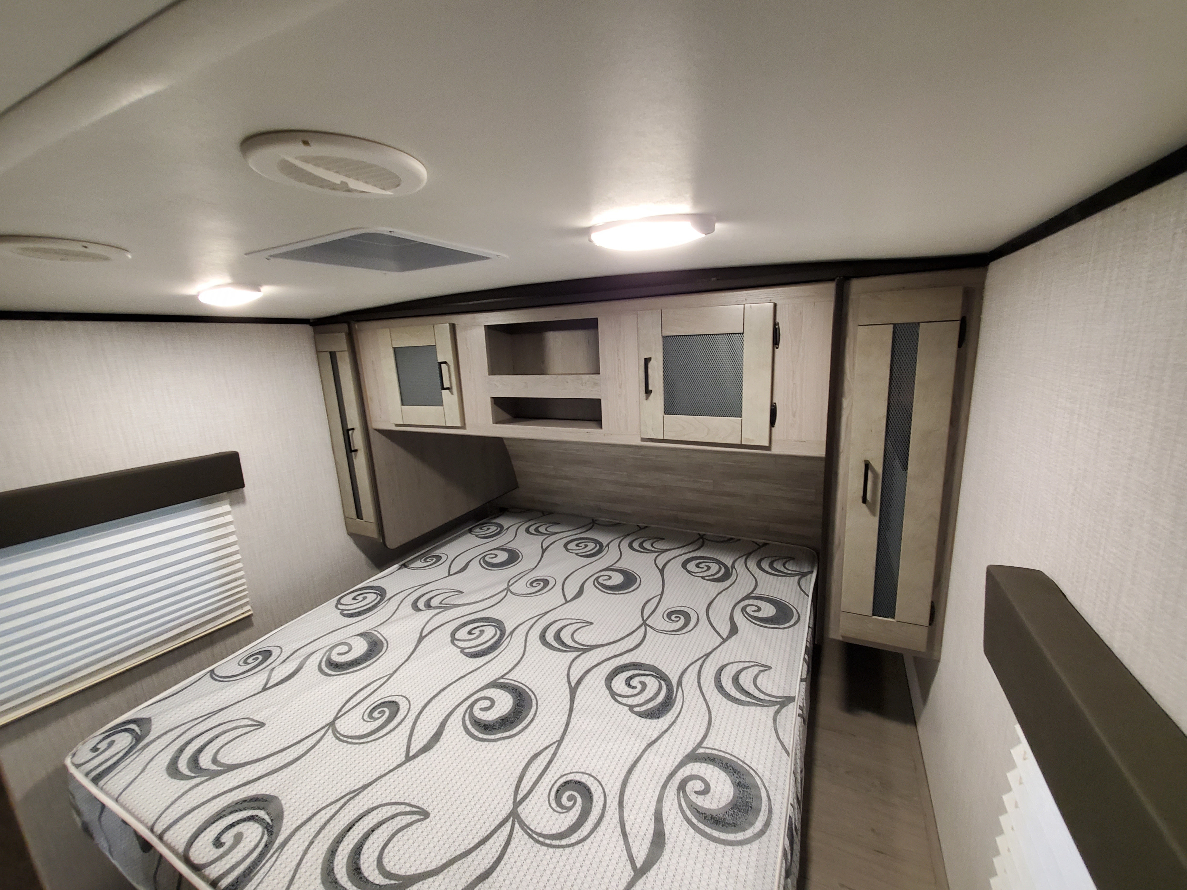 Inside an RV rental bedroom: light wood cabinets, patterned mattress on bed, ceiling lights & vents. Cozy and functional.. Heartland Mallard m26 2021