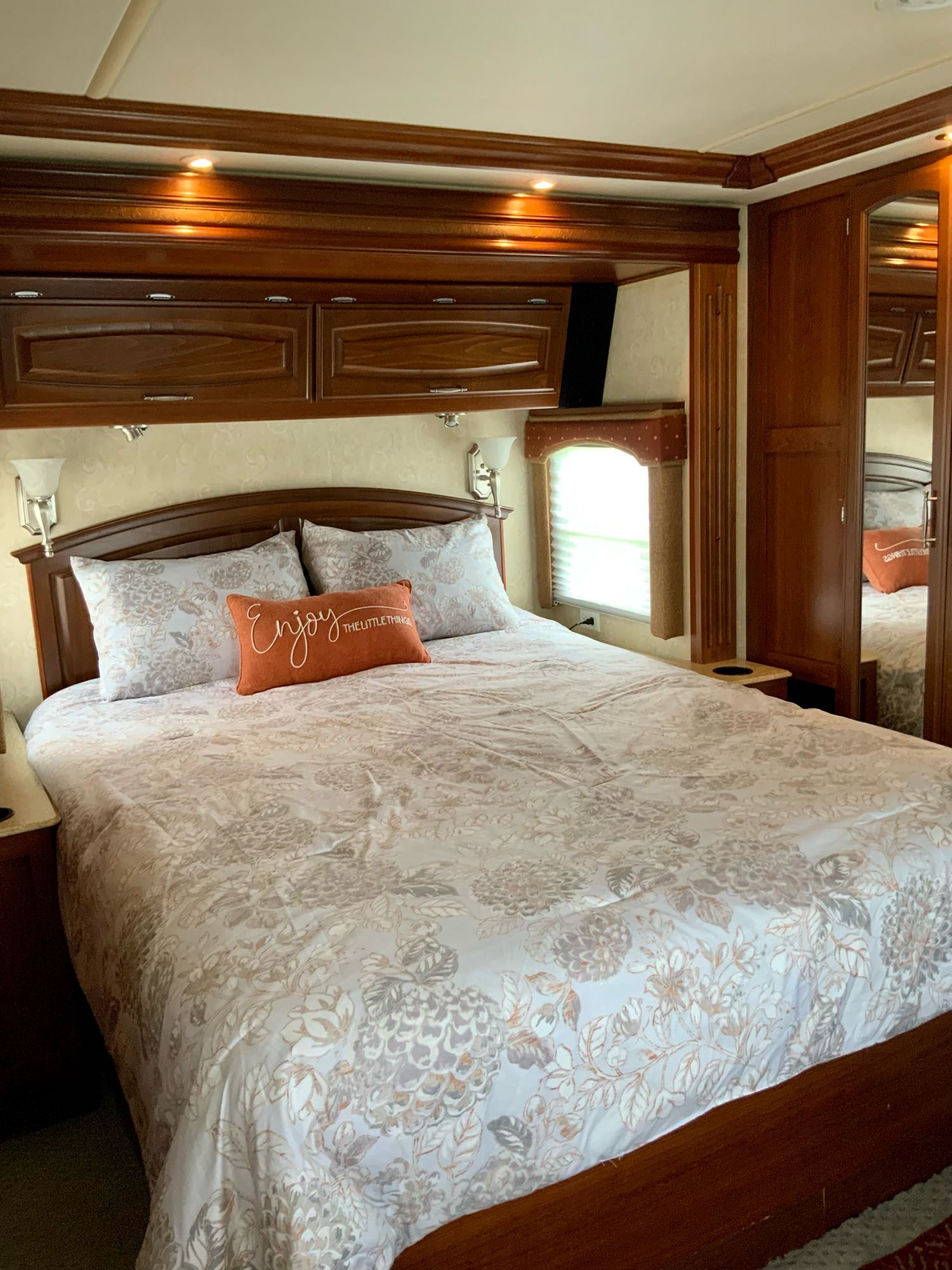 Cozy RV rental bedroom featuring a comfortable bed with floral bedding, wooden cabinetry, and overhead lighting. Ideal for travel.. Fleetwood Excursion 2008