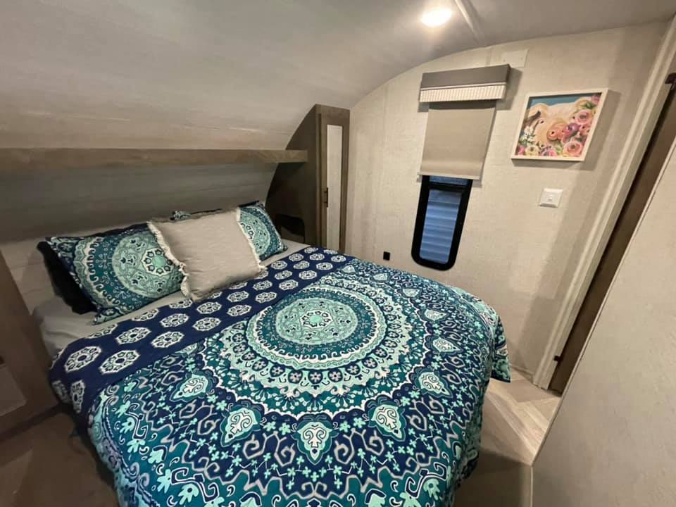 RV rental bedroom featuring a bed with a vibrant blue and teal mandala comforter, small window, and wall art.. Forest River Salem Cruise Lite 2021