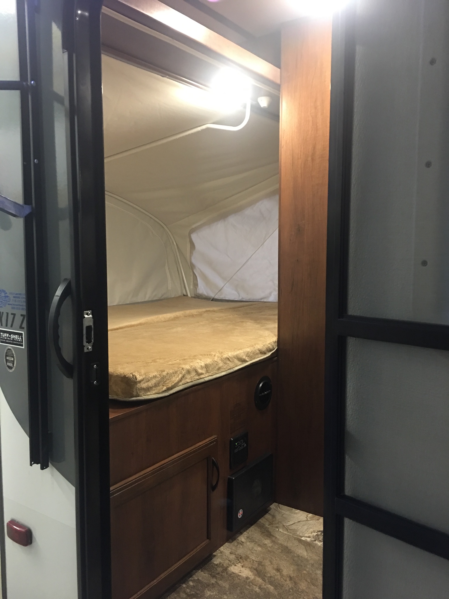 This RV rental interior features a cozy pop-up camper bed with a light, controls, and an open entry door.. Jayco Jay Feather 2016