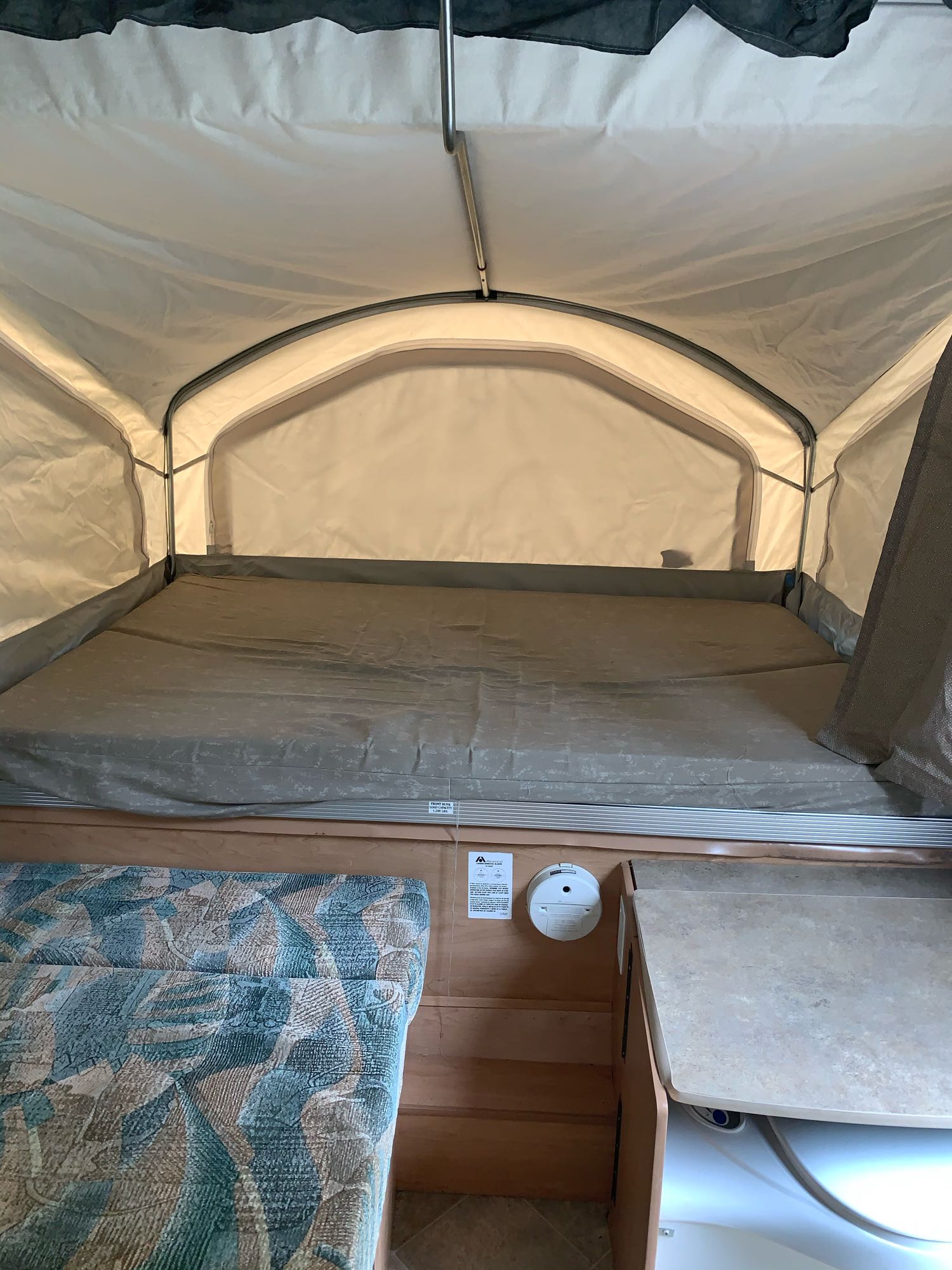 Inside a pop-up RV rental, featuring a spacious bed, light fabric walls, and a small built-in counter area.. Coachmen Sport 2007