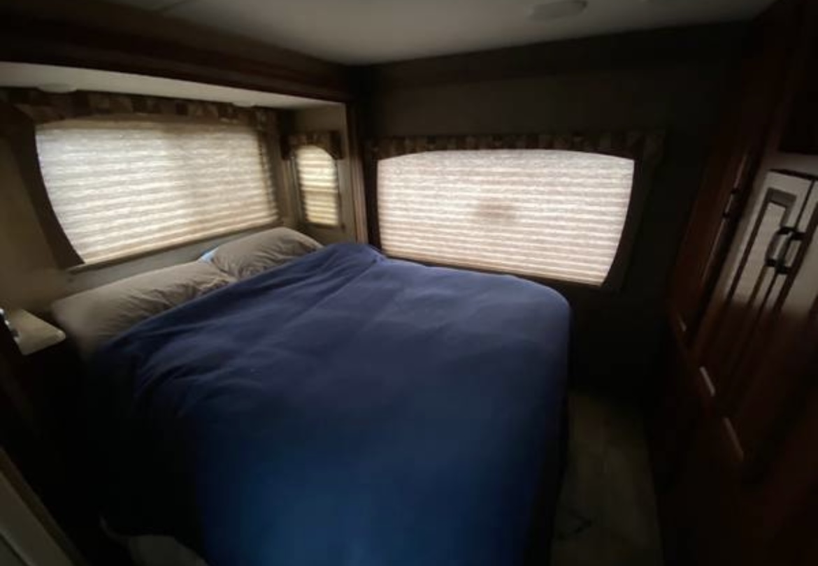 RV rental bedroom: a cozy space with blue blanket, pillows, and windows with blinds.. Forest River Sunseeker 2016
