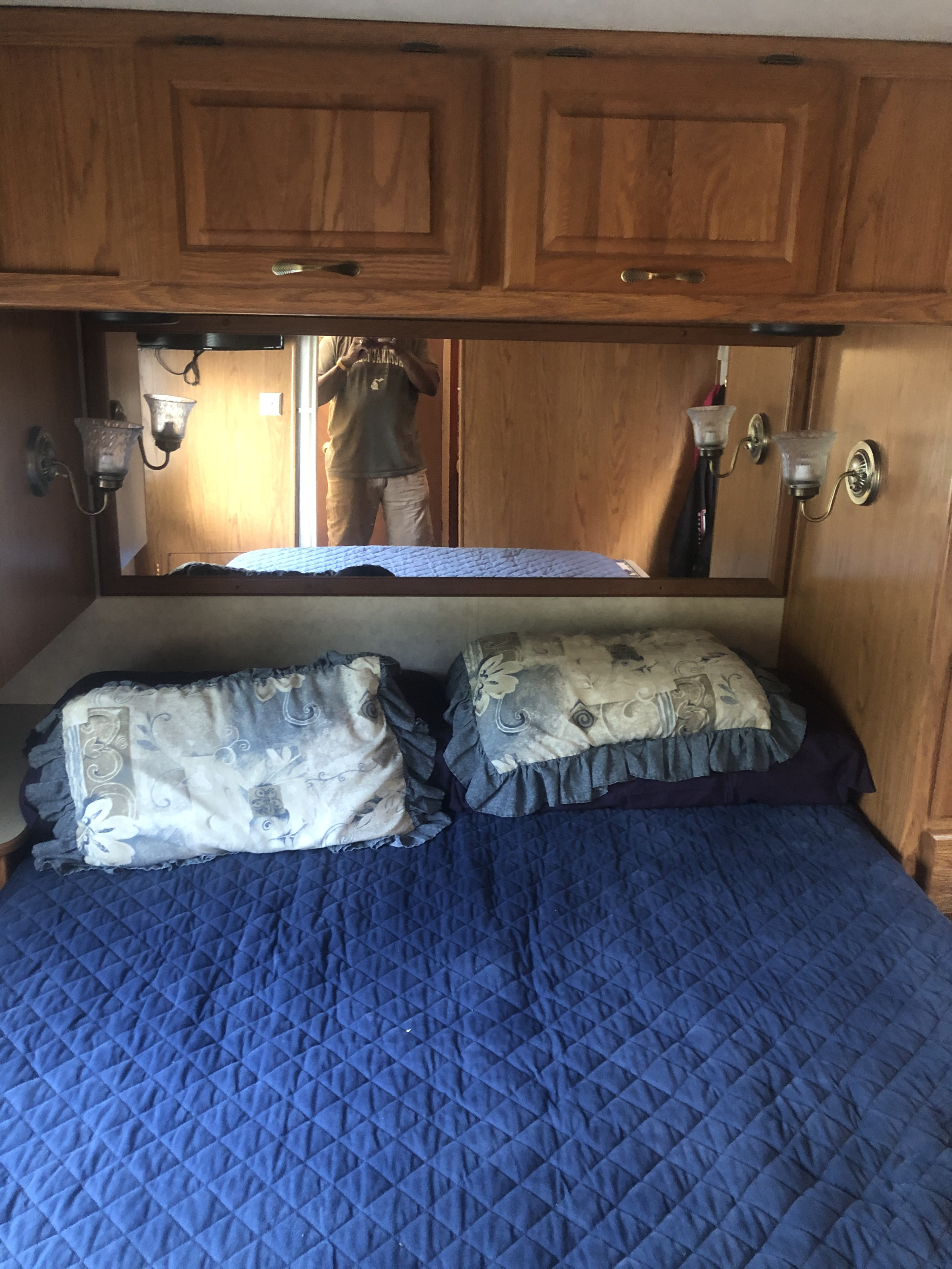 Cozy RV rental bedroom with a blue quilted bed and overhead cabinets. Mirror reflects the interior and person.. Damon Daybreak 2005