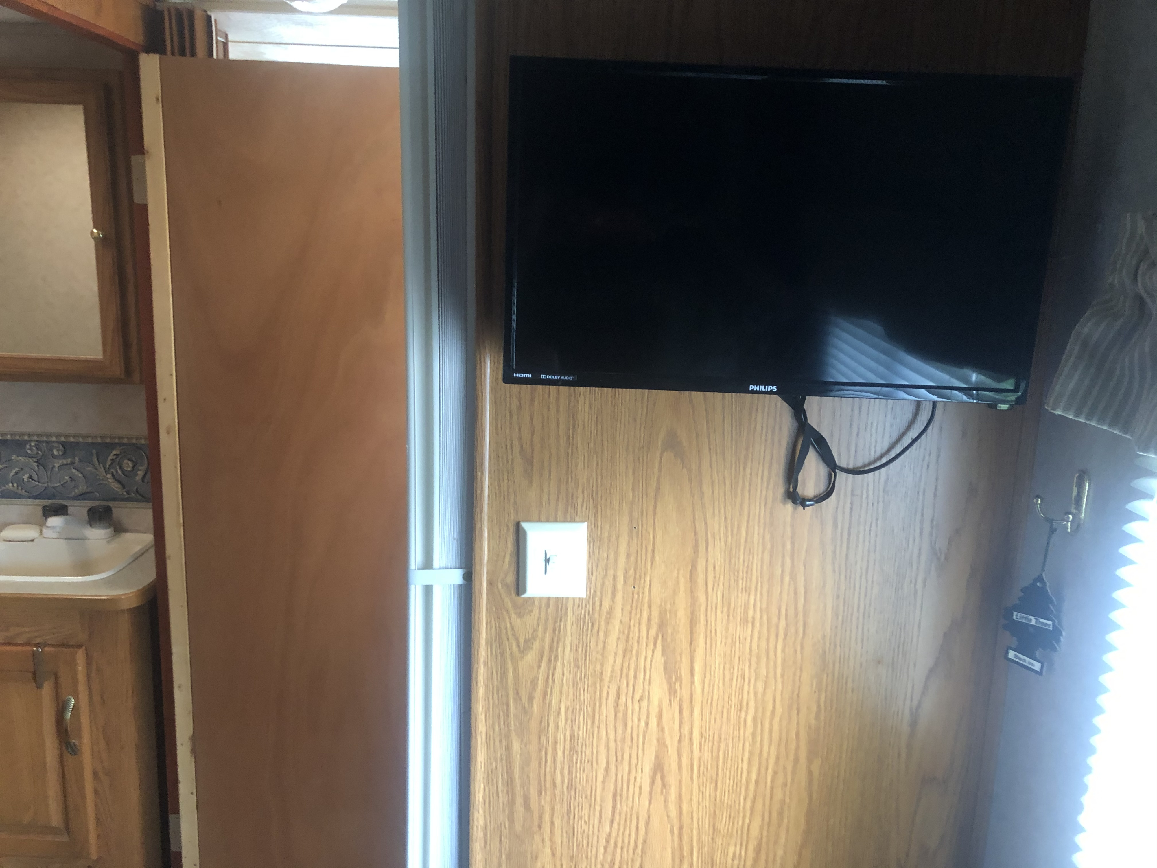 RV rental interior: wood-paneled wall with a Philips TV, a compact bathroom sink, and a space-saving sliding door.. Damon Daybreak 2005