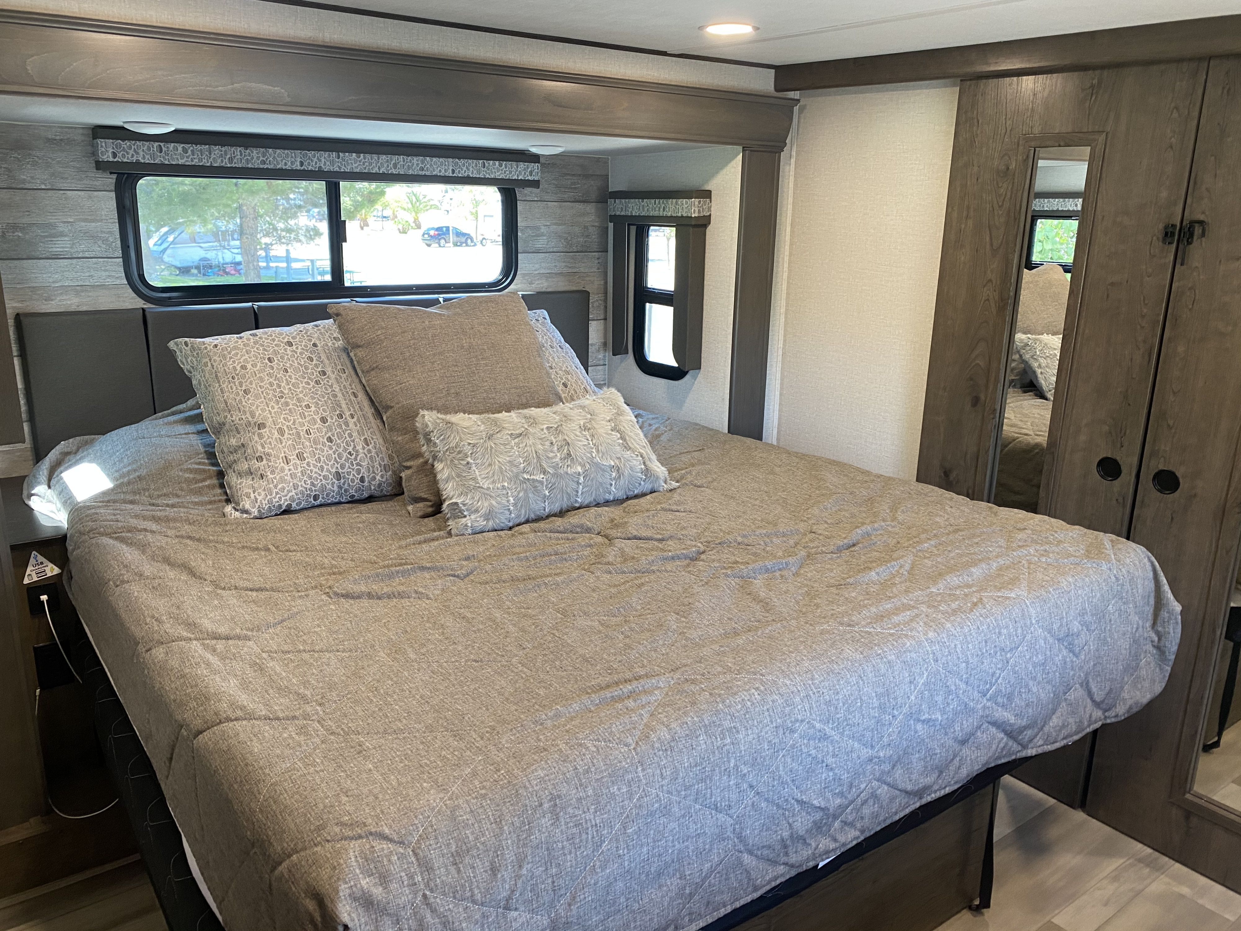 This inviting RV rental bedroom offers a comfortable bed, windows with outdoor views, and practical storage solutions.. Alliance RV Paradigm 2021