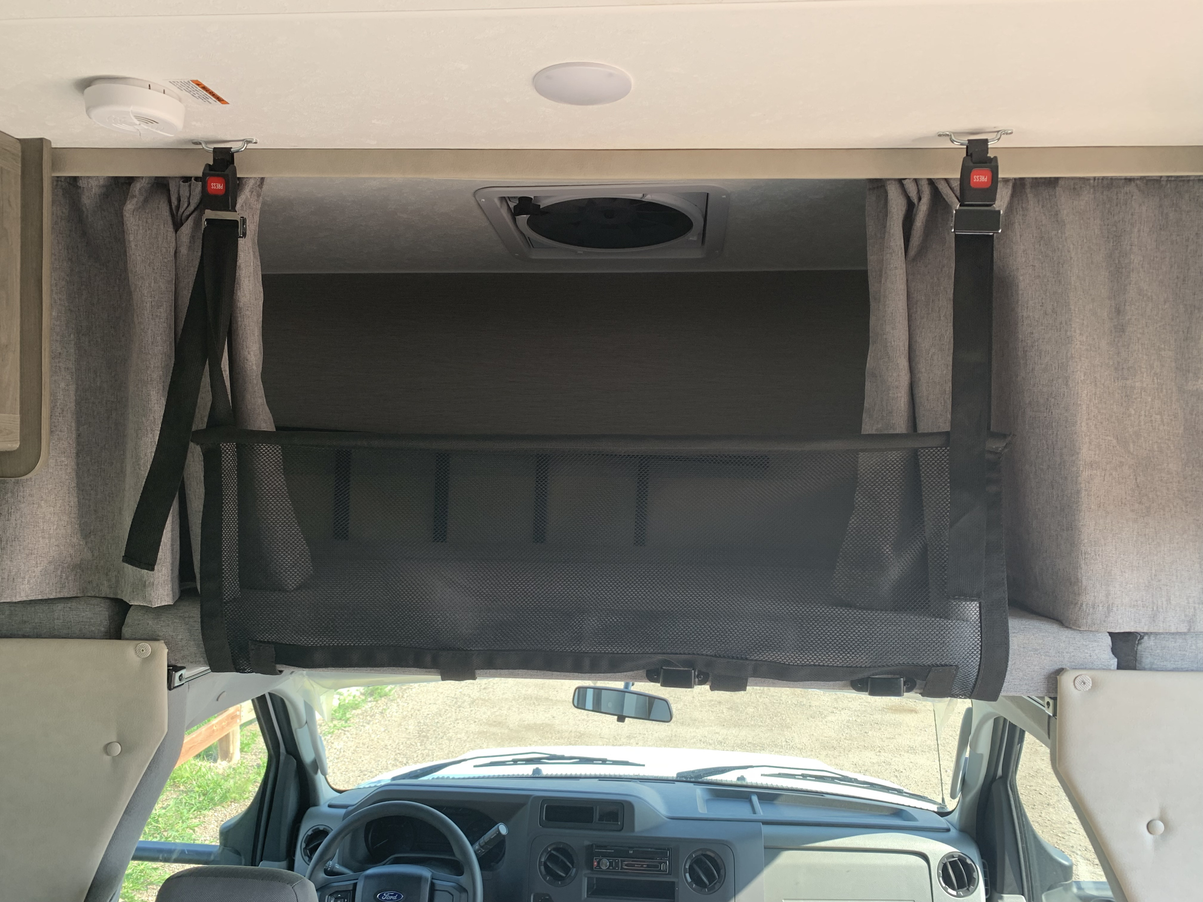 Inside an RV rental, a black mesh safety net spans the overhead bunk, secured by red-buckled straps, with a smoke detector above.. Other Other 2021
