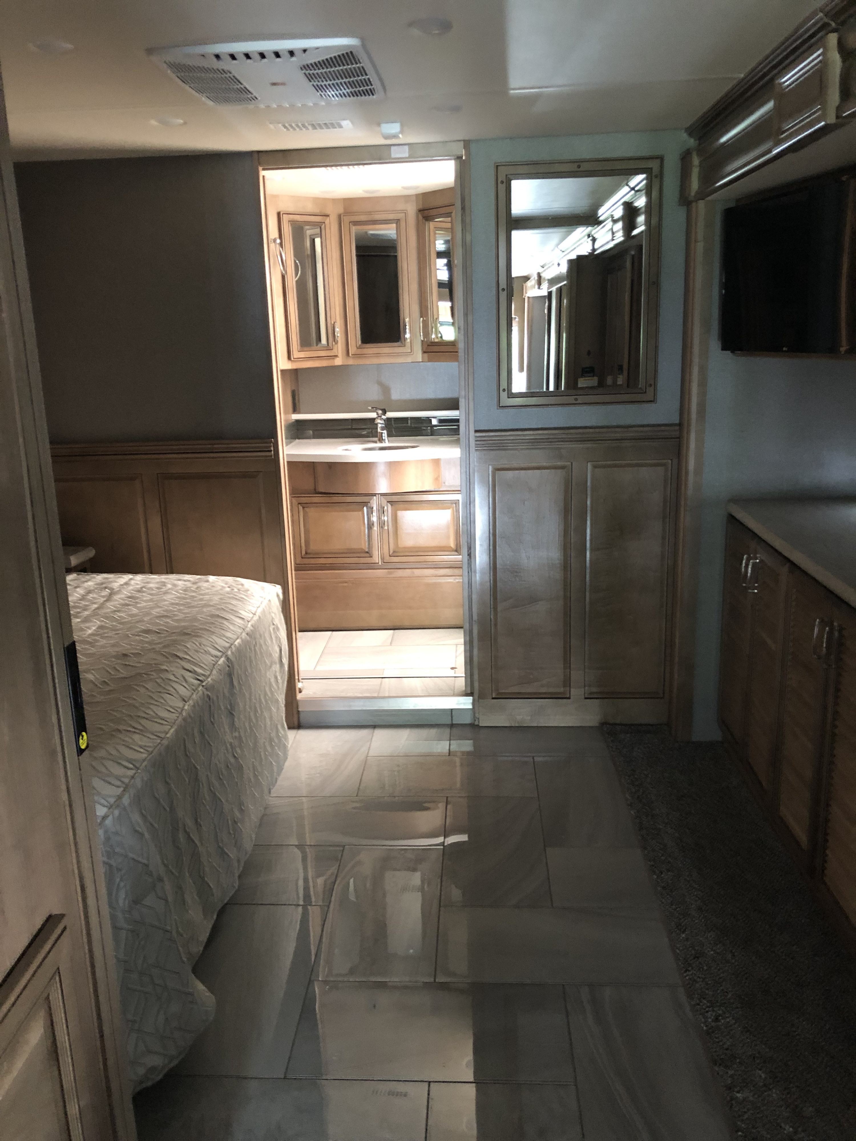 RV rental interior: bedroom, light wood paneling, glossy tile floor, and a mirrored bathroom vanity with a sink.. Fleetwood Discovery 2019