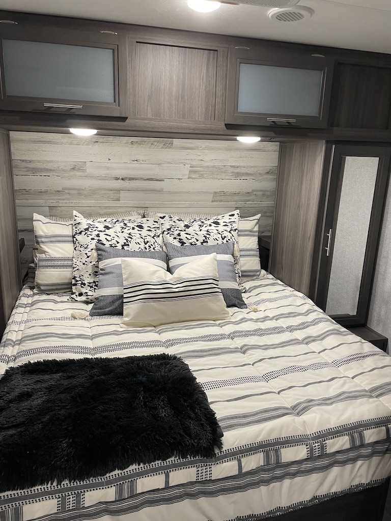Cozy RV rental bedroom featuring striped bedding, overhead cabinets, and a mirrored closet for a comfortable stay.. Dutchman Kodiak Ultra-Lite 2021