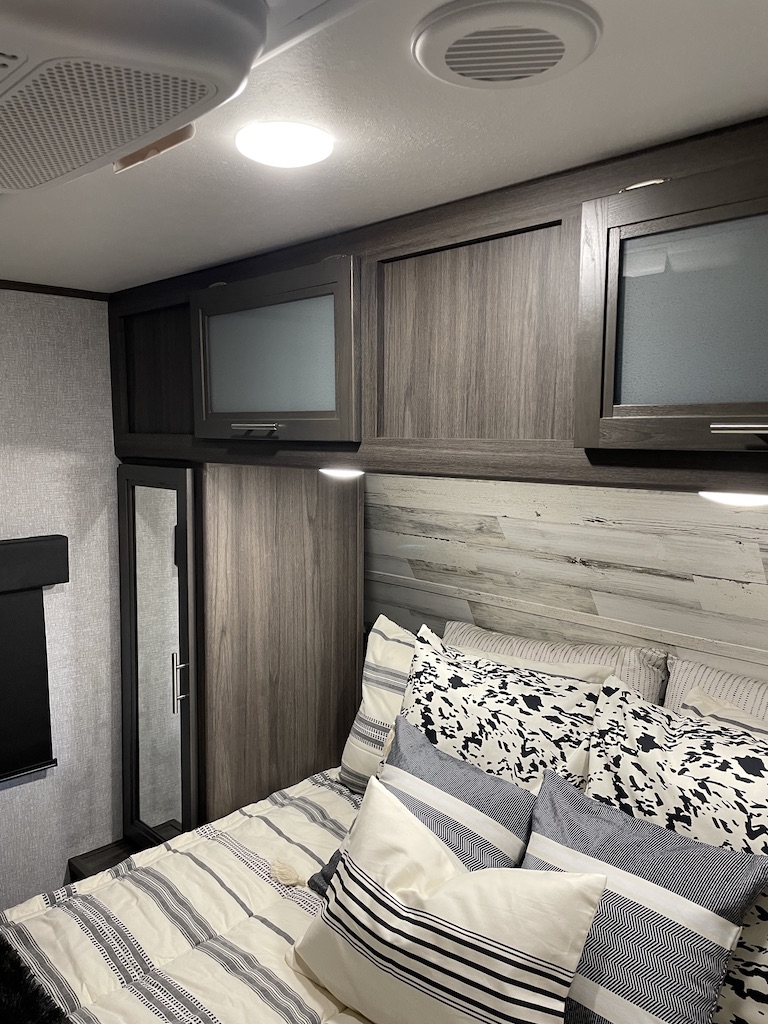Relax in this comfortable RV rental bedroom, featuring stylish bedding, modern overhead cabinets, and a mirrored wardrobe.. Dutchman Kodiak Ultra-Lite 2021