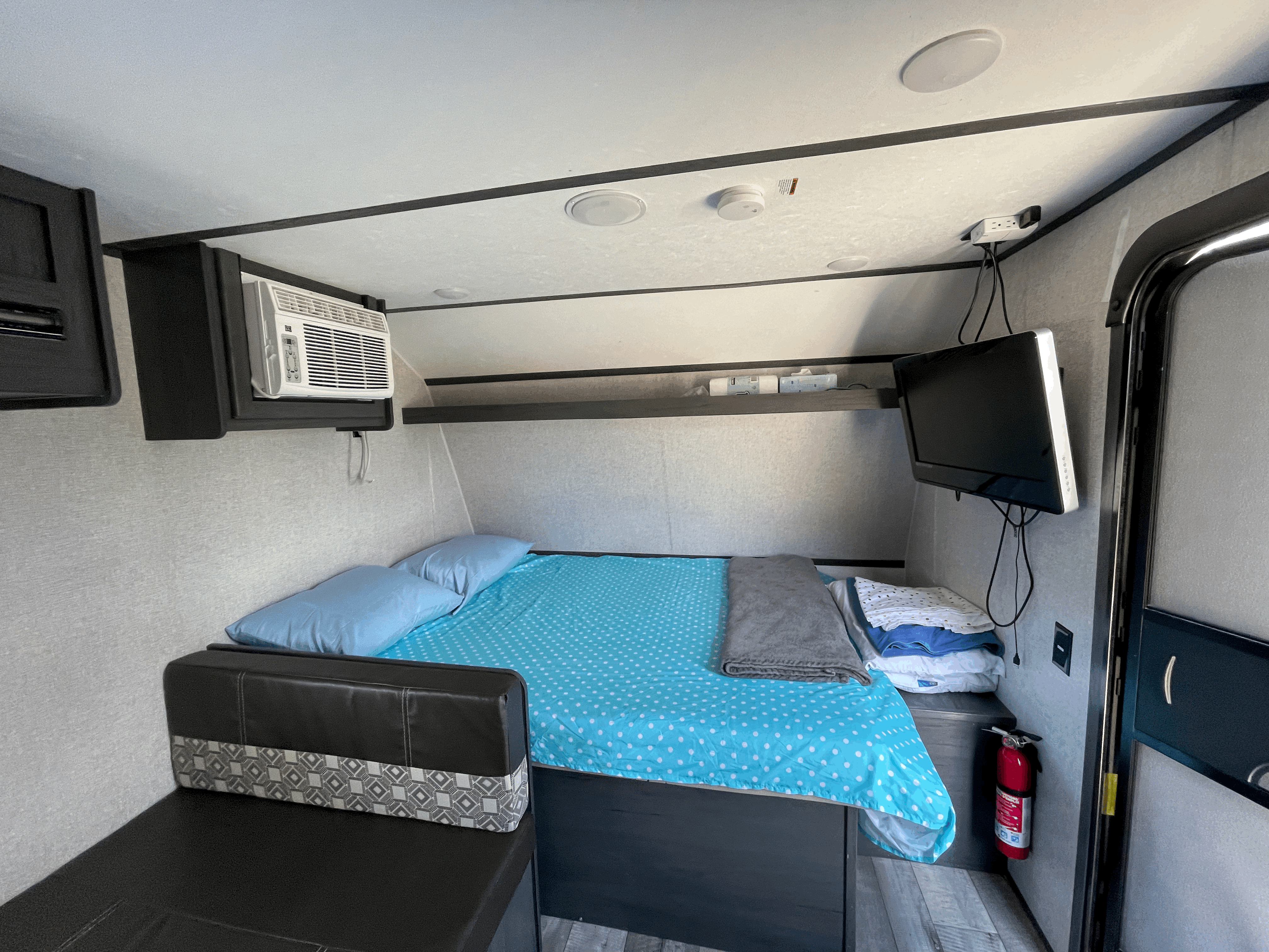 Cozy rv rental interior featuring a functional bedroom with a bed, AC, TV, and fire extinguisher.. Dutchmen Aspen Trail 2021