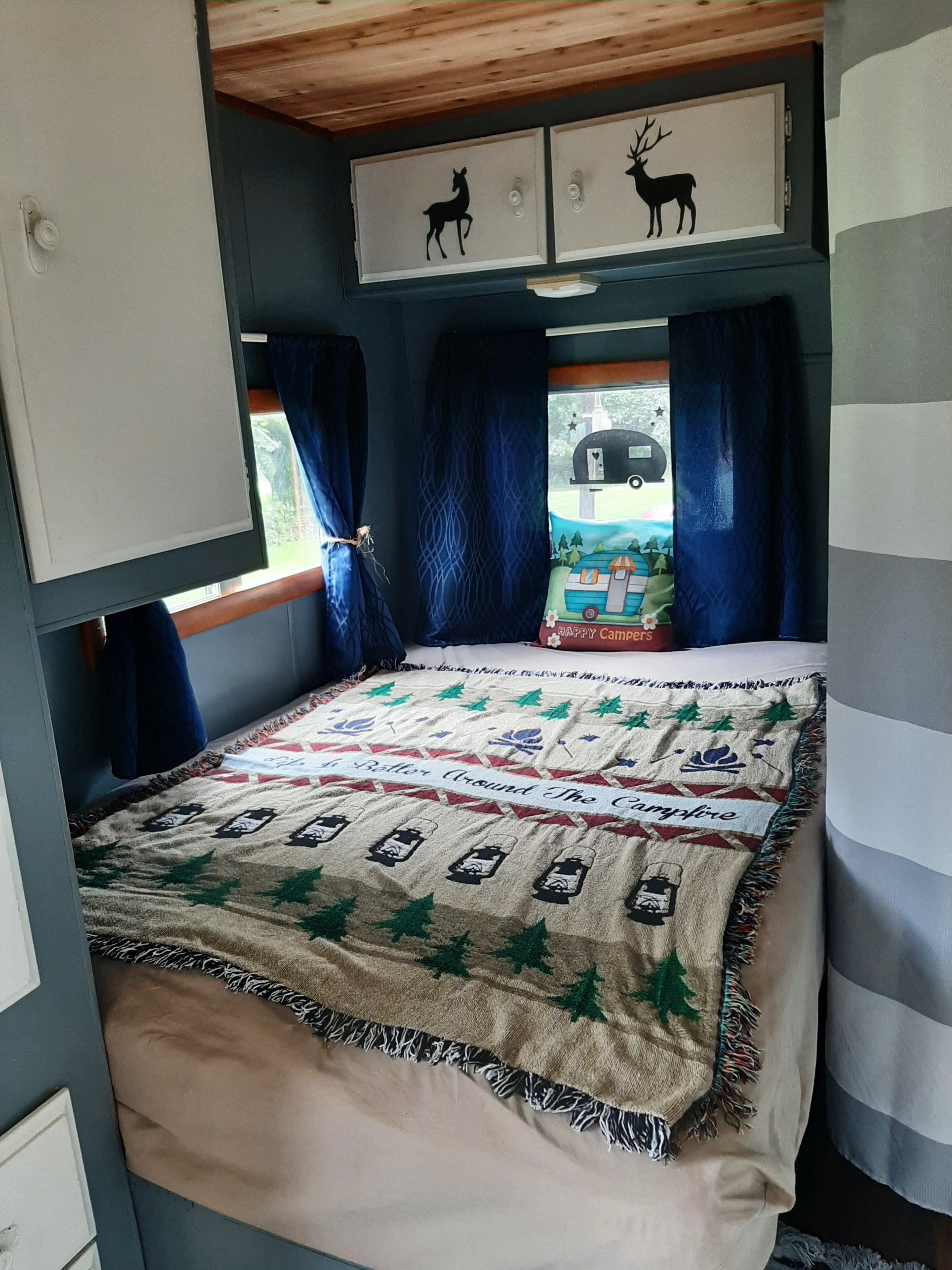 Cozy RV rental bedroom with a camping-themed blanket, deer decor cabinets, and blue curtains, perfect for a getaway.. Fleetwood Wilderness 1990