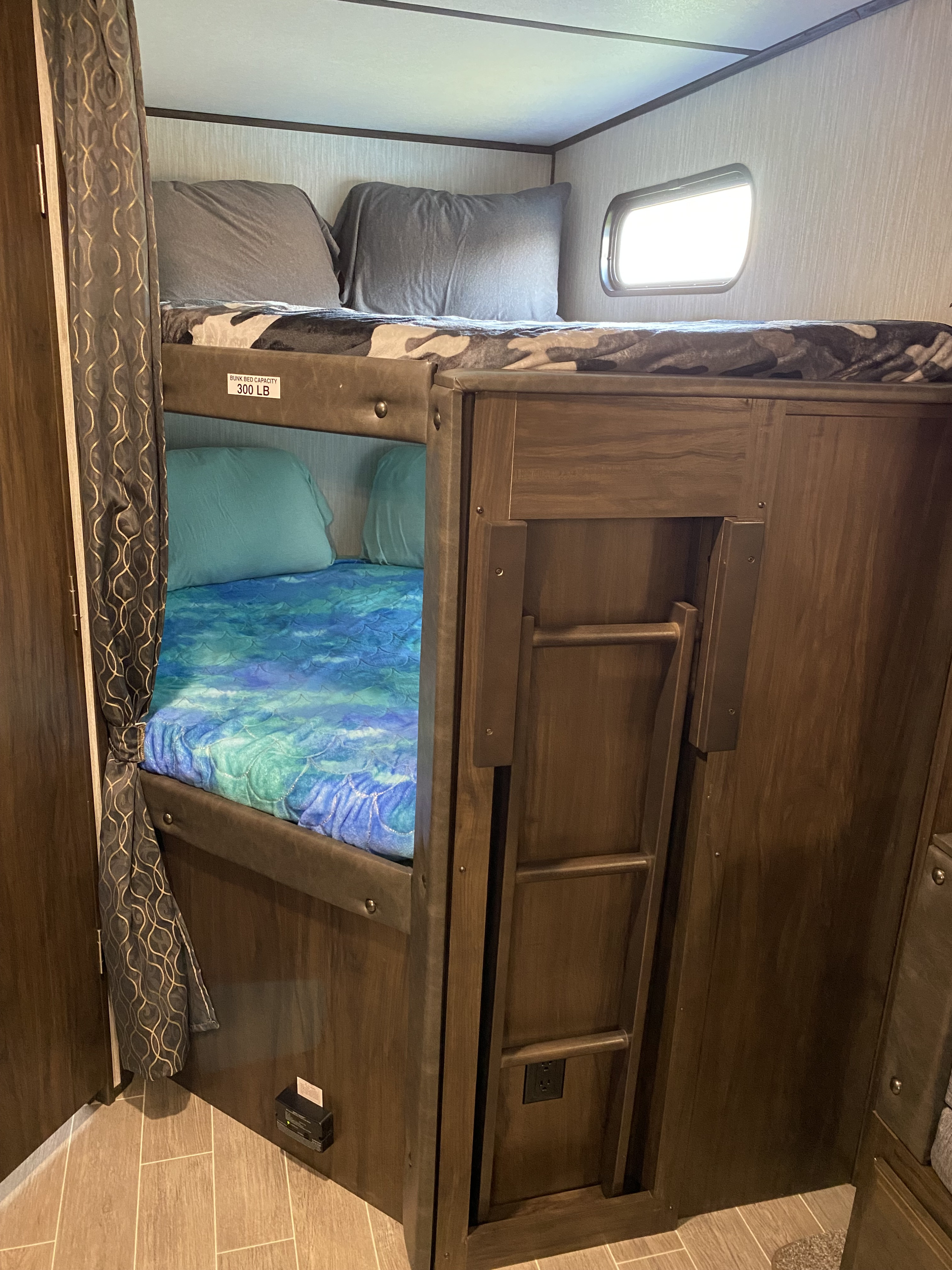 Inside an RV rental: two cozy bunk beds with different bedding designs and an attached ladder, ideal for family camping.. Forest River Alpha Wolf 2020