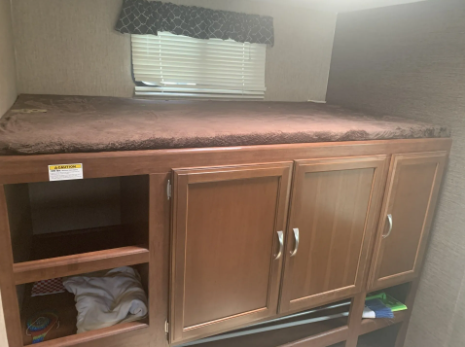 RV rental interior: cozy bunk bed above wooden storage with open shelves and closed cabinets, ideal for family trips.. Keystone Passport 2017
