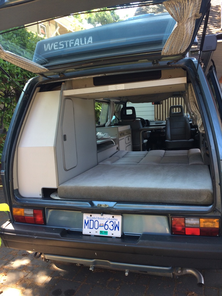 Ready for adventure! This well-equipped Westfalia camper van interior shows the comfortable bed & compact kitchen, perfect for an RV rental. British Columbia plate seen.. Volkswagen T3 Westfalia 1988