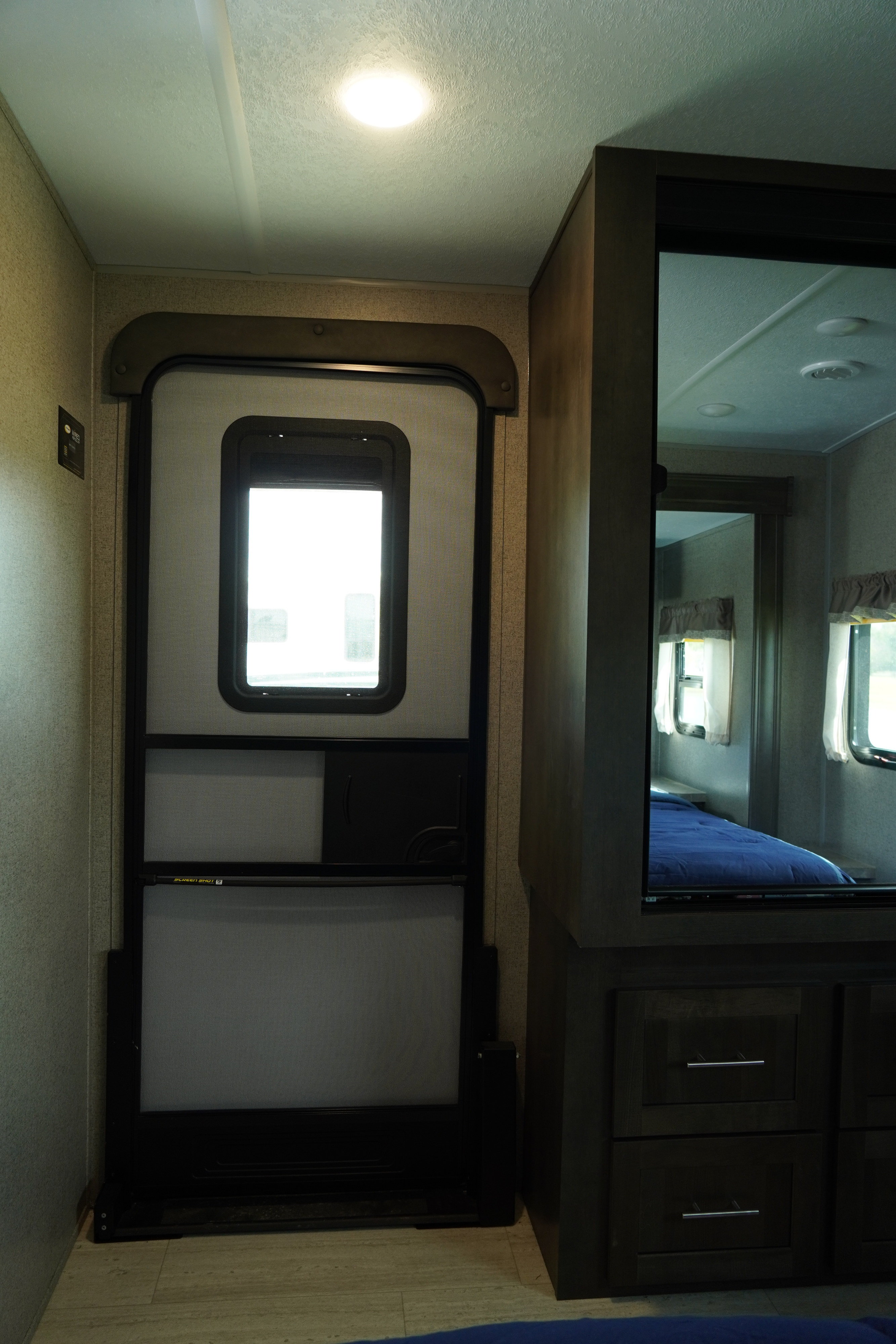 RV rental interior featuring a screen entry door, overhead lighting, and a mirrored partition revealing the compact bedroom.. Forest River Flagstaff Super Lite 2021