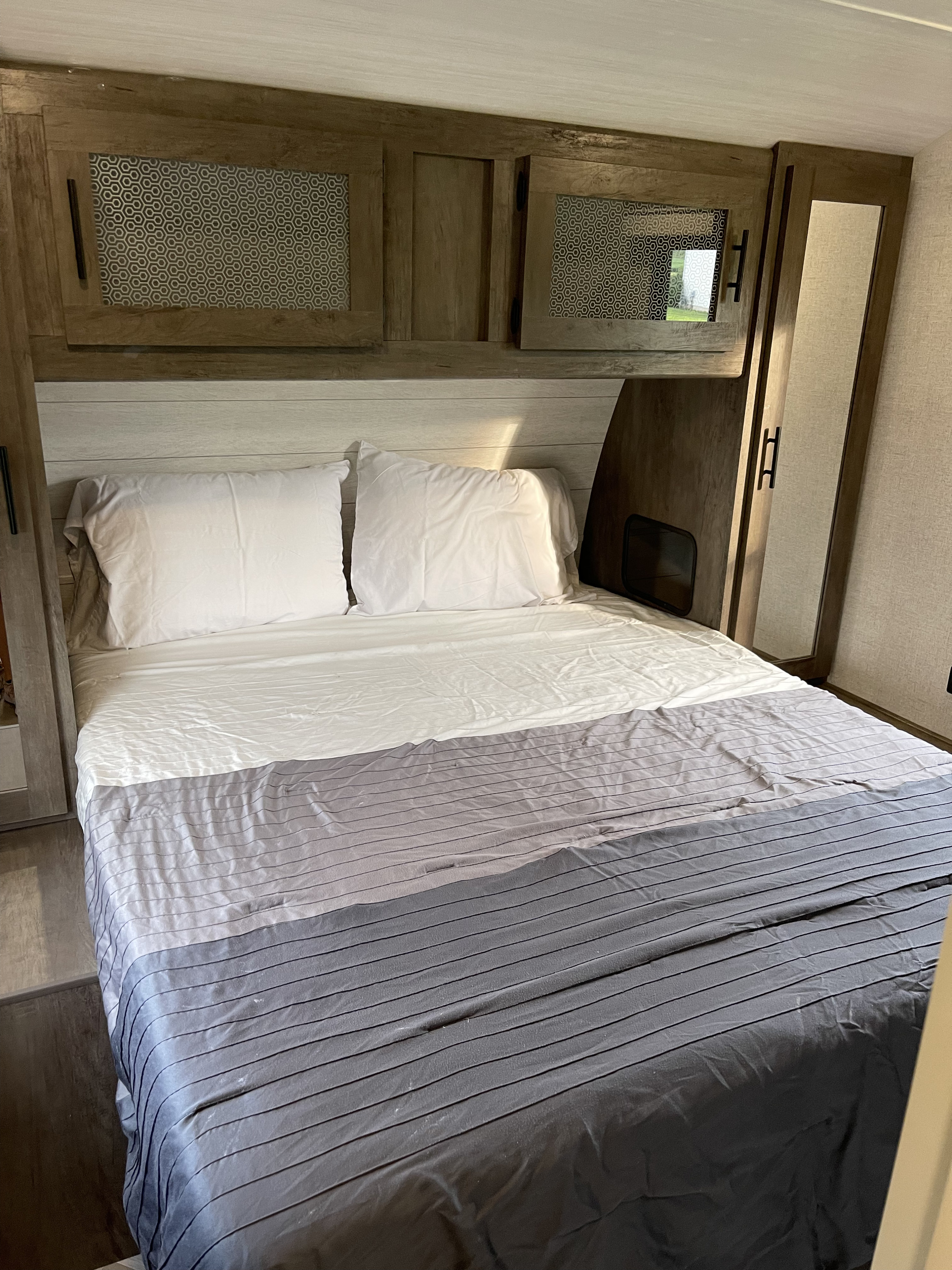 Cozy RV rental bedroom featuring wood cabinets with honeycomb accents, mirrored storage, and a comfy bed with striped bedding.. Forest River Wildwood 2021