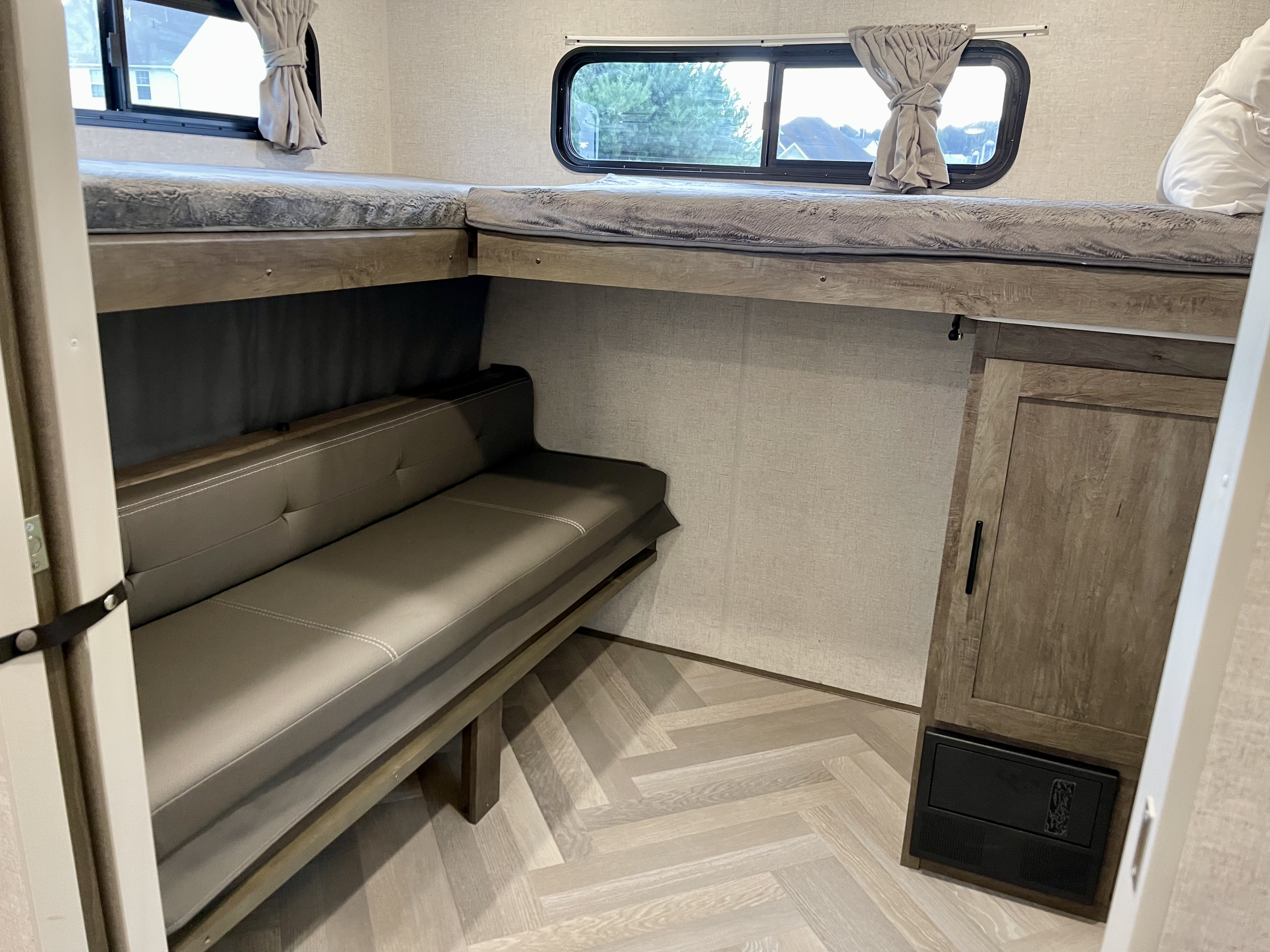 Modern RV rental interior: L-shaped bunk beds, cozy dinette, windows, and light flooring create a functional space.. Forest River Wildwood 2021