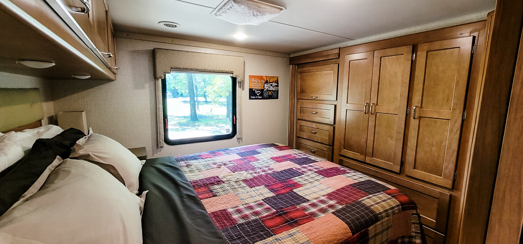 Cozy RV rental bedroom featuring a patchwork quilt bed, window with trees, and ample wooden storage. Ideal for travelers.. Winnebago Minnie Winnie 2018