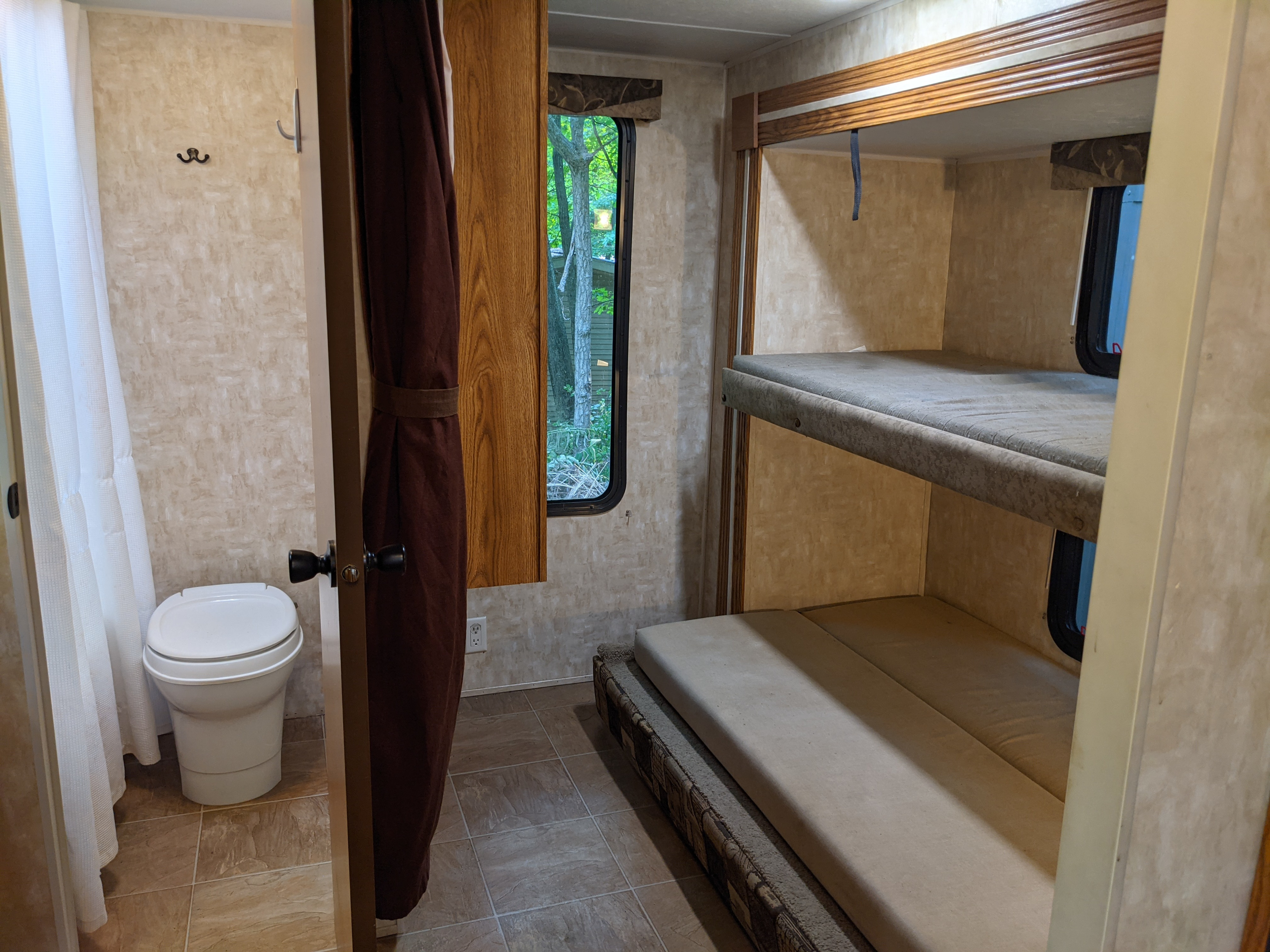 RV rental interior: bunk beds, windows looking out to green trees, and a compact bathroom with toilet and shower curtain.. Forest River Cherokee Lite 2006