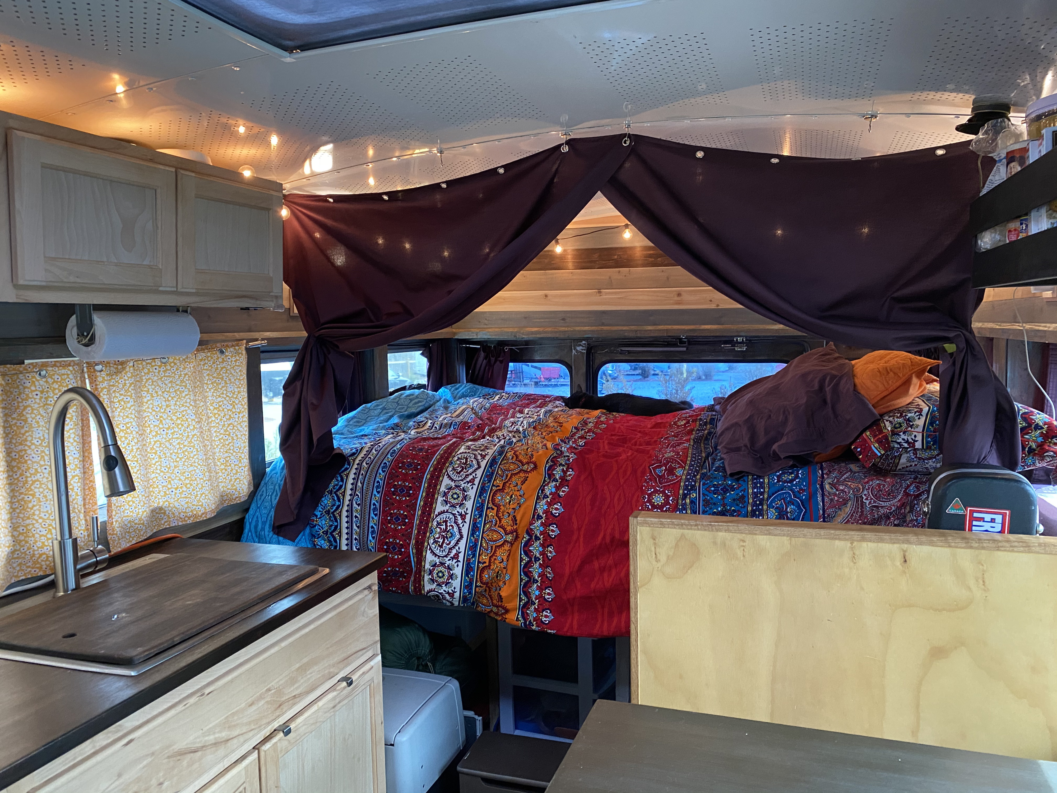 This cozy RV rental interior features a vibrant bed, kitchen, string lights, and a sleeping cat, ideal for adventure.. Ford E450 2005