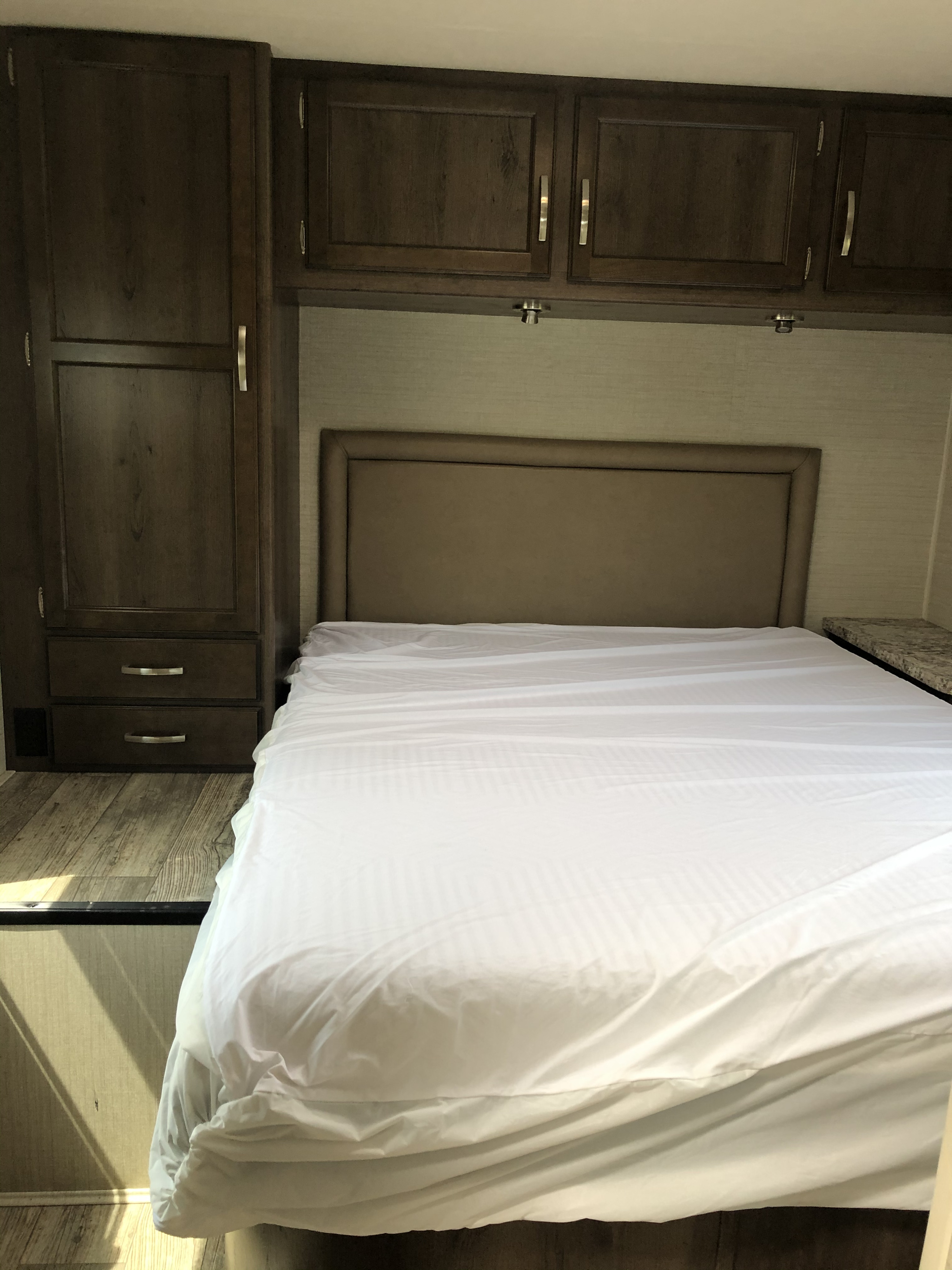 Cozy RV rental bedroom features a neatly made bed, ample dark wood storage cabinets, and a comfortable headboard.. Jayco Redhawk 2018