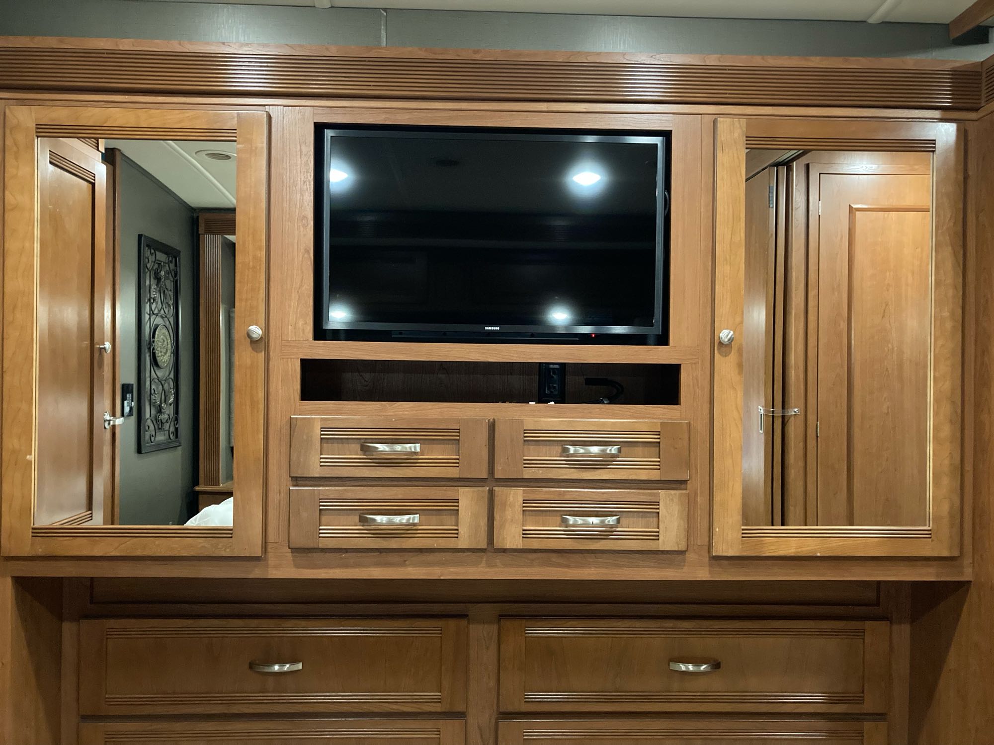 RV rental bedroom cabinet featuring a flat-screen TV, reflective wardrobe doors, and multiple storage drawers.. Winnebago Forza 2018