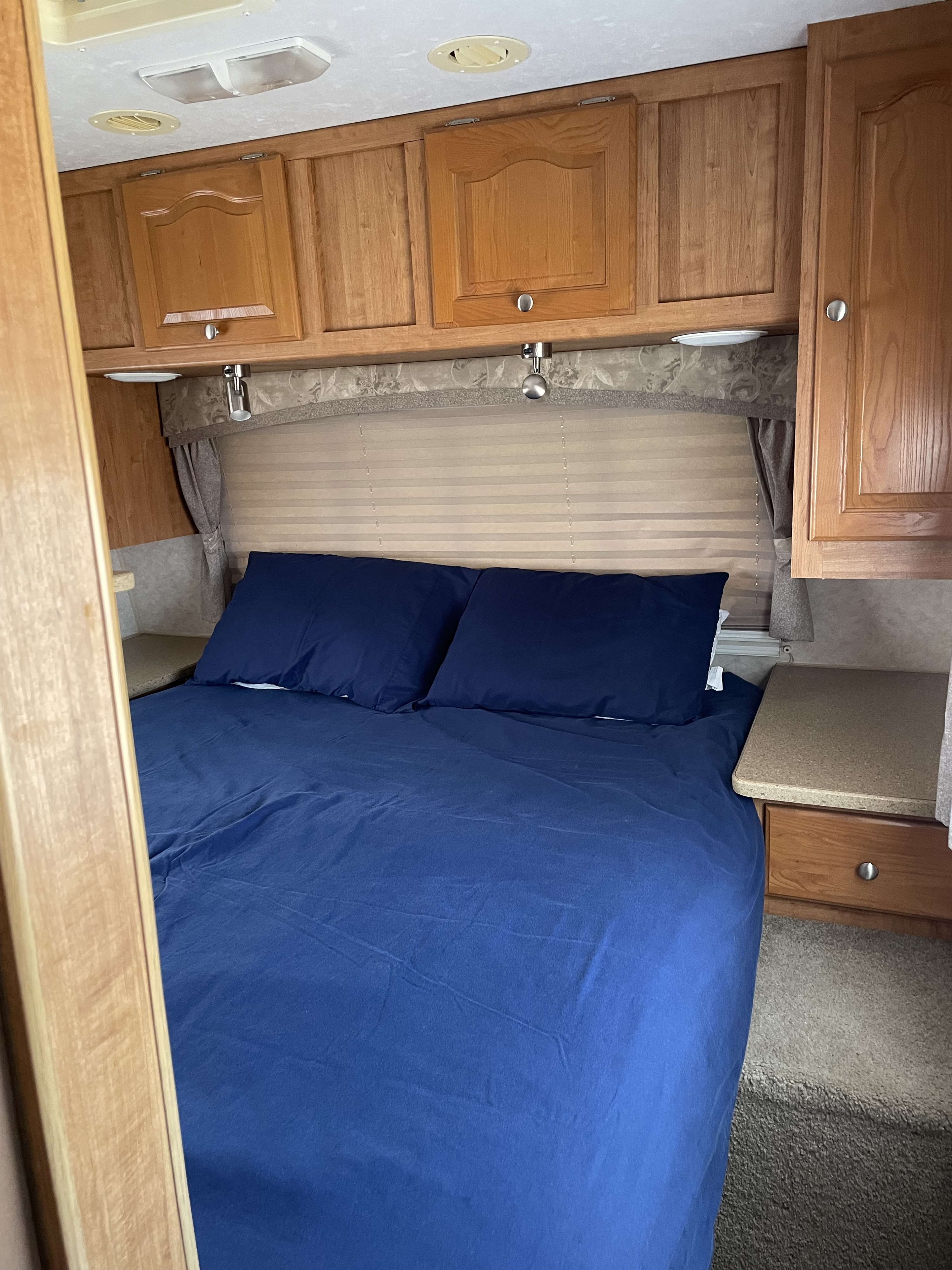 Cozy RV rental bedroom featuring blue bedding, overhead cabinets, and built-in lighting. Perfect for comfortable travel.. Forest River Rockwood Lite 2007