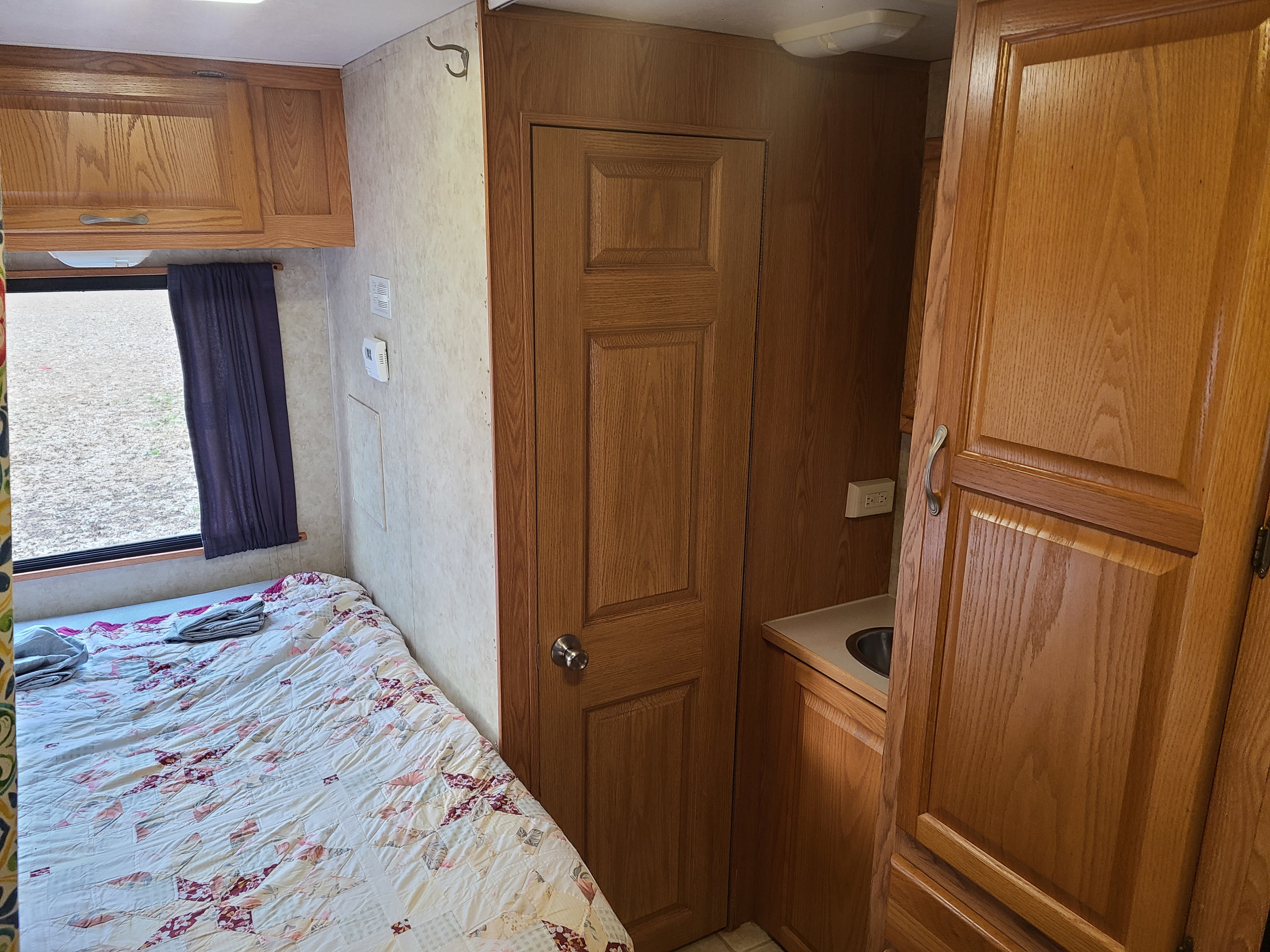 RV rental interior with a patterned bed, window, and light wood cabinetry featuring a compact sink area.. Other Four Winds Majestic 2006