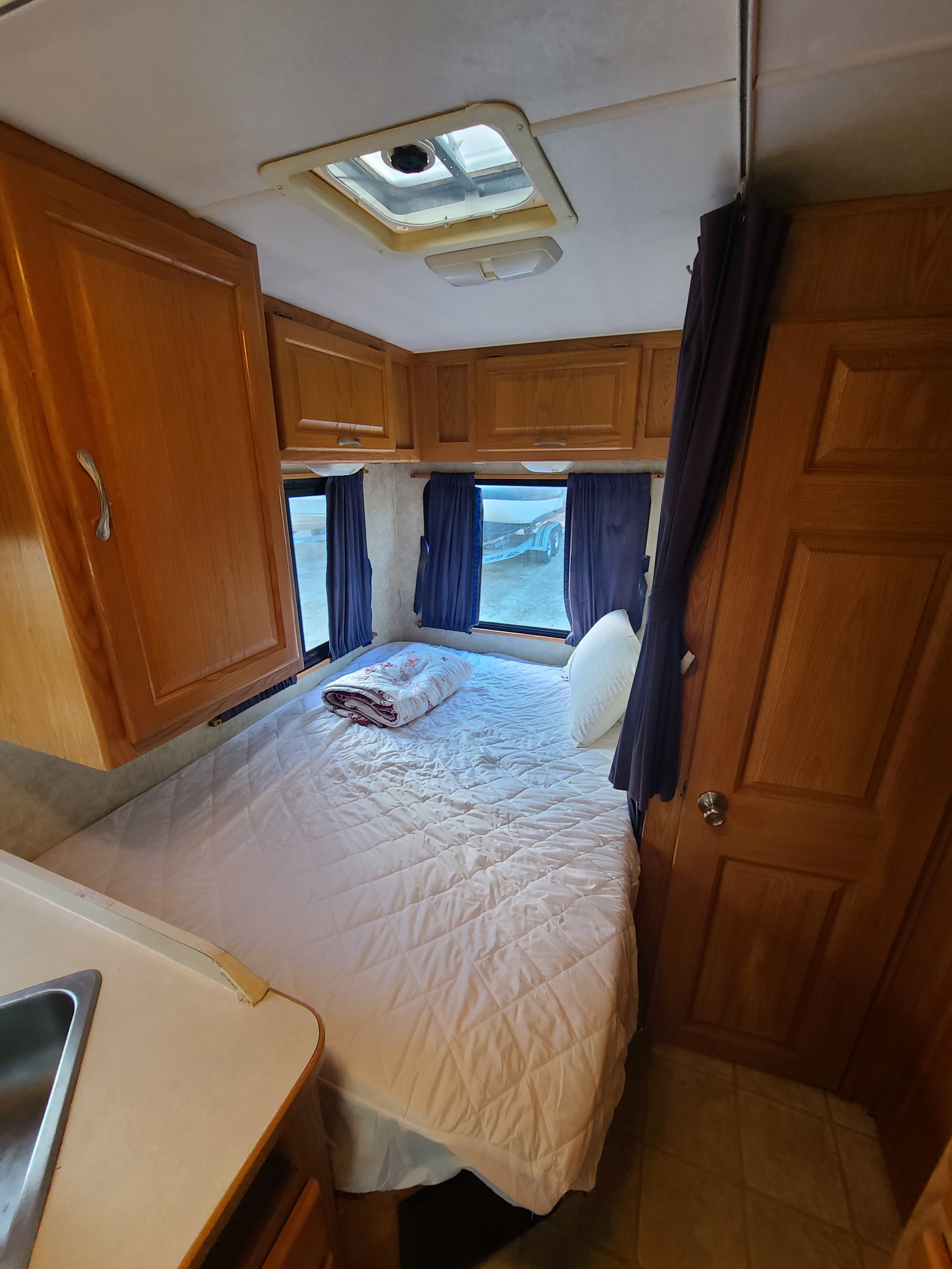 RV rental interior features a tidy bedroom with a quilted bed, wood cabinets, and large windows with privacy curtains.. Other Four Winds Majestic 2006
