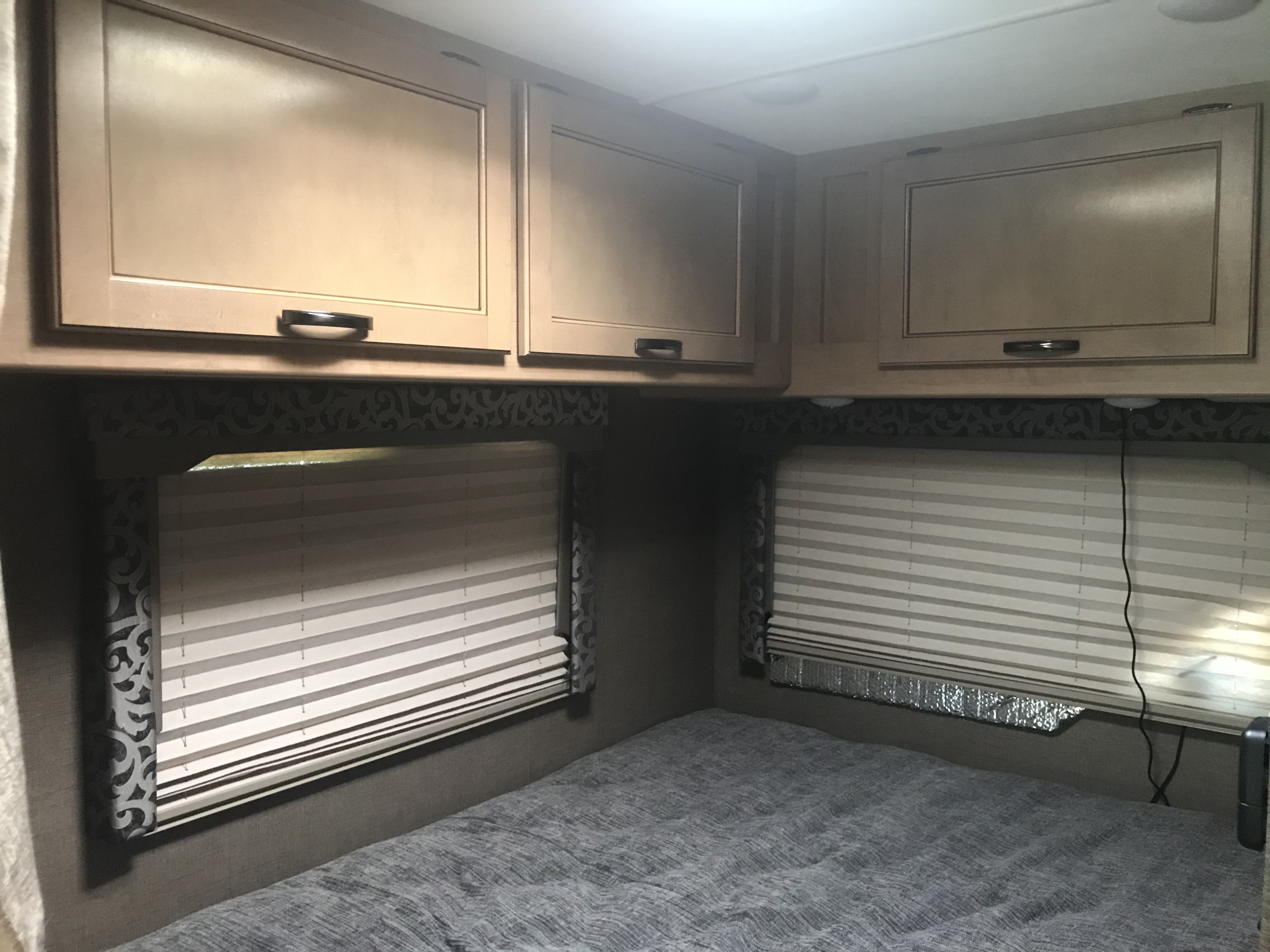 RV rental bedroom interior featuring light cabinets, two windows with blinds, and a grey bed with textured bedding.. Thor Four Winds 2019
