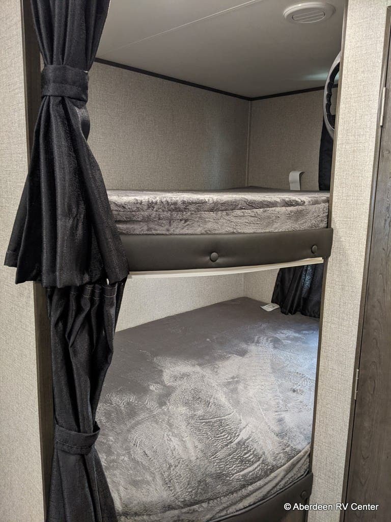 An RV rental features two cozy bunk beds with gray mattresses and privacy curtains, perfect for extra sleeping.. Jayco jay flight 2021