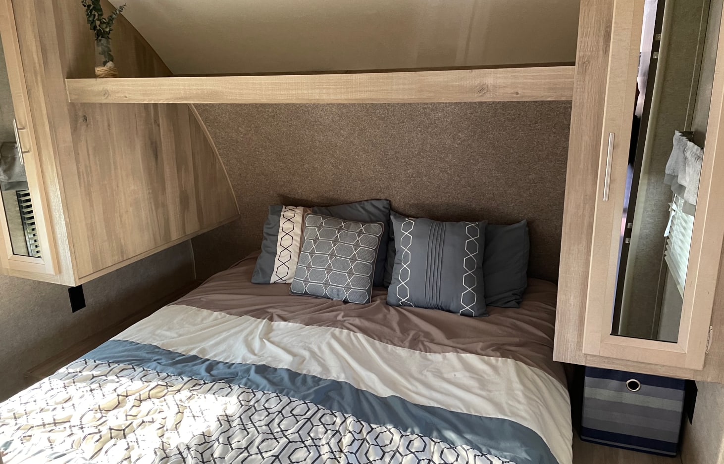 Cozy RV rental bedroom featuring patterned bedding, decorative pillows, and practical overhead storage cabinets.. Coachmen Catalina 2020