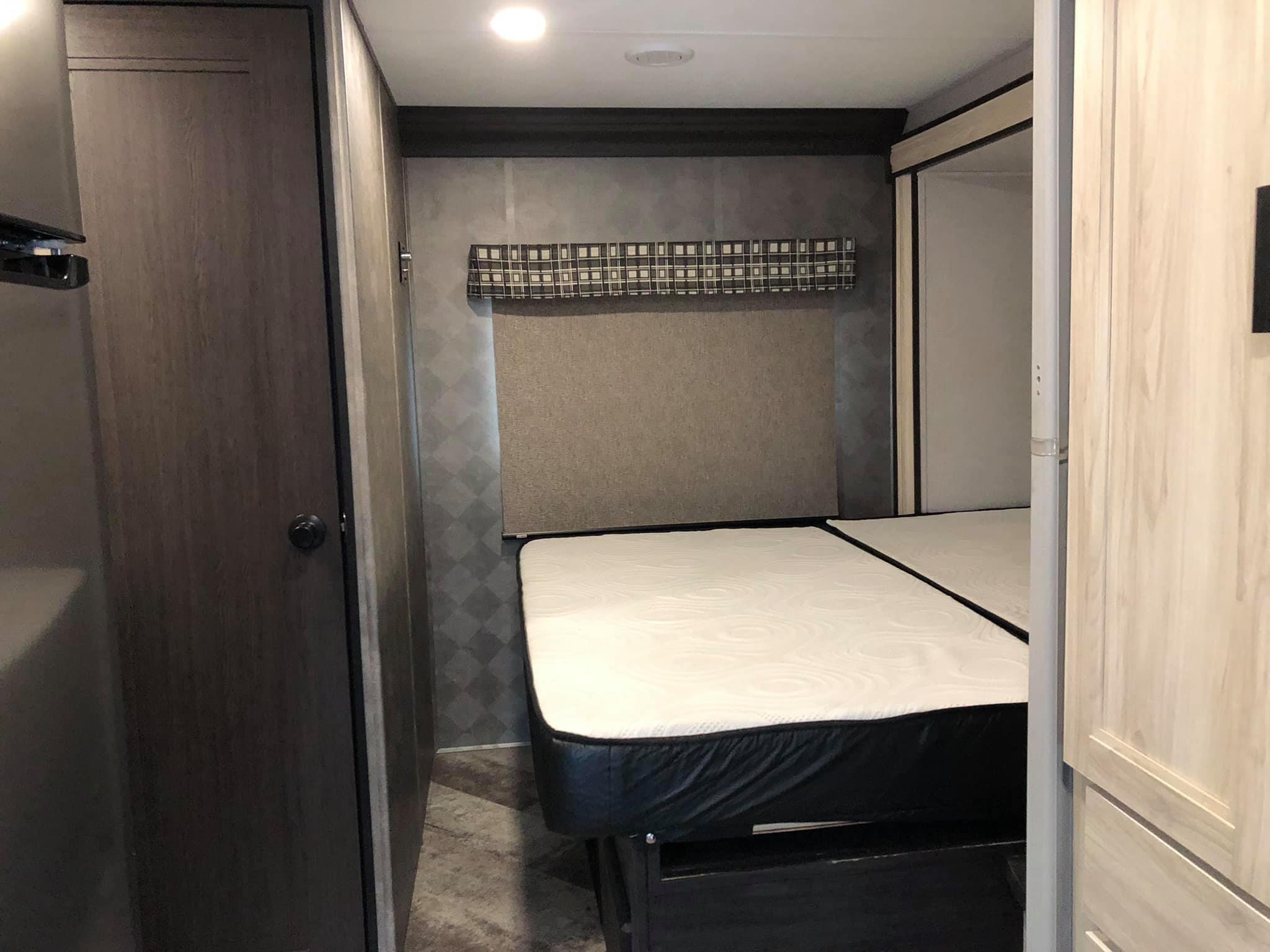 Compact RV rental bedroom featuring a white mattress on a dark base, patterned walls, and wood-paneled doors.. Forest River Sunseeker 2021