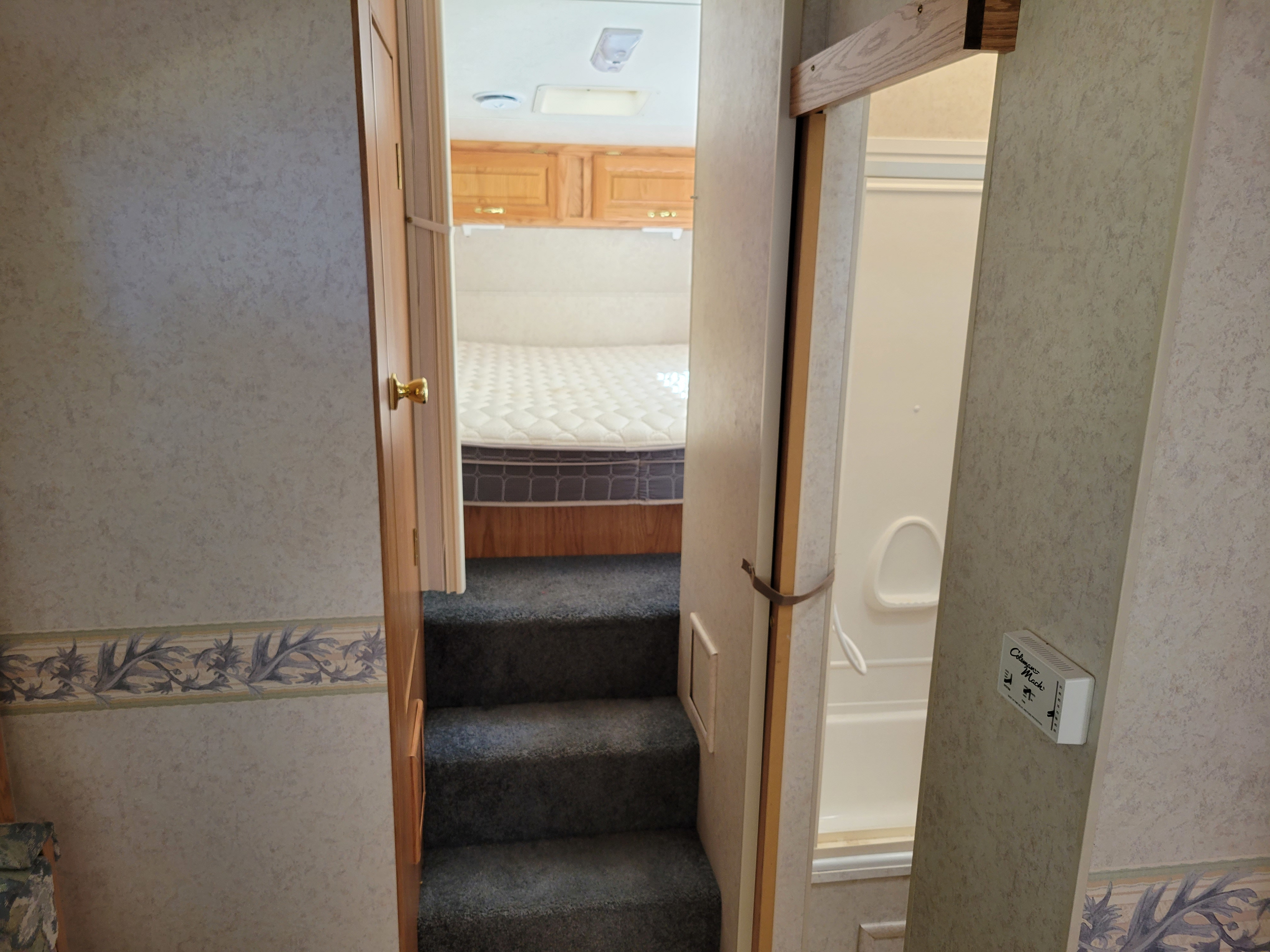 This RV rental interior shows steps leading to a bedroom with wooden cabinets, with a bathroom visible to the right, featuring a Coleman Mach unit.. Jayco Eagle 2002